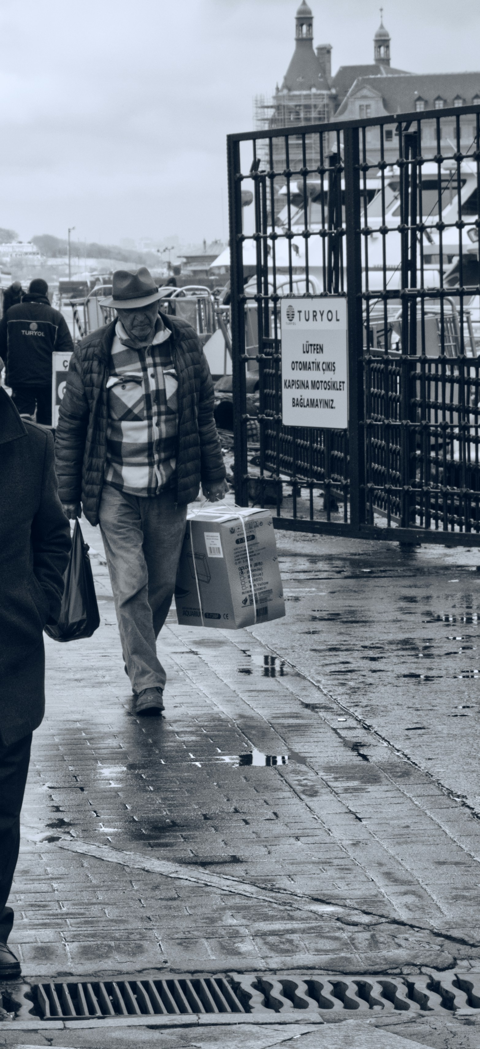 L'uomo con il cappello porta scatole sul marciapiede bagnato