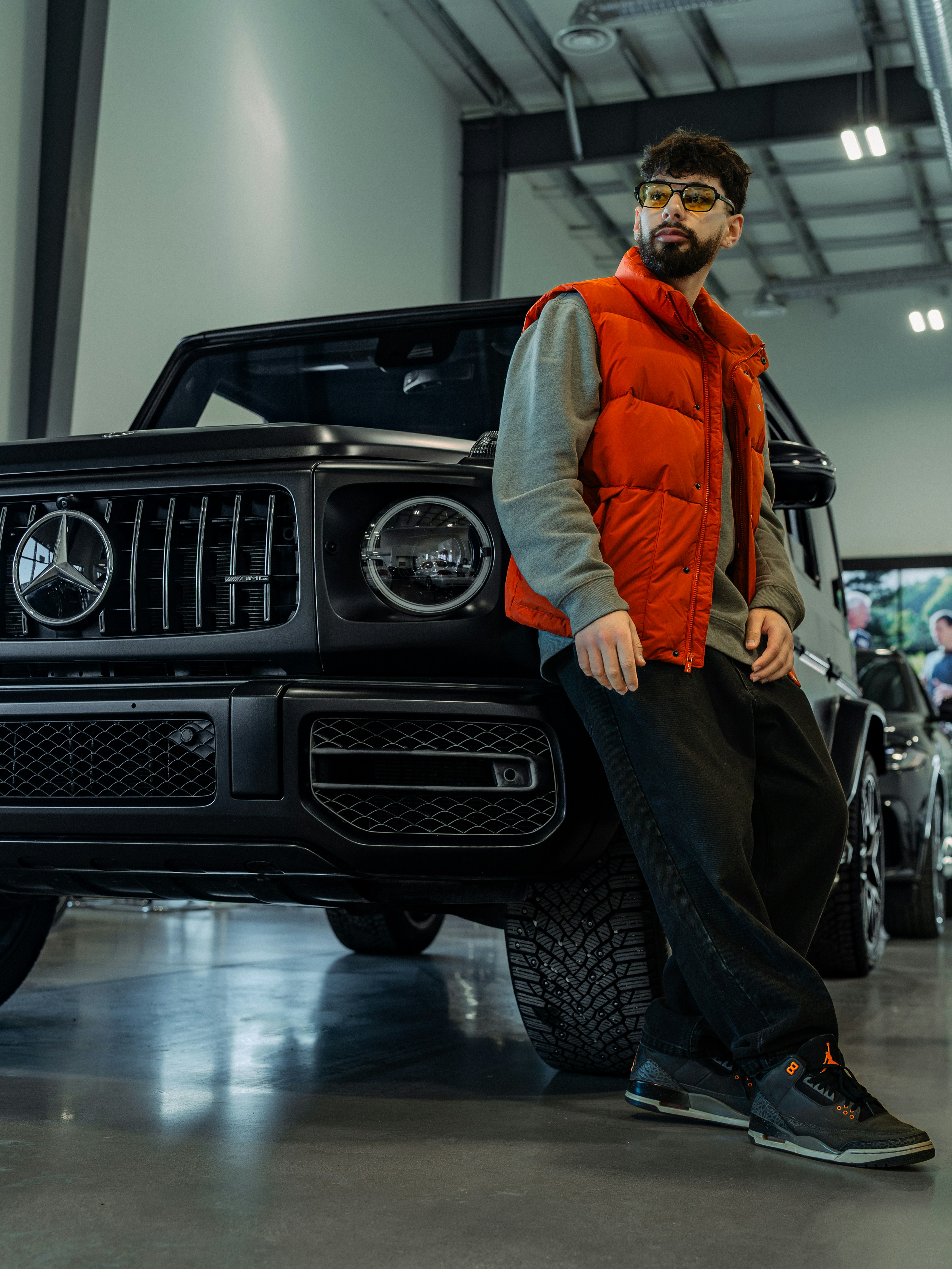 Man in puffer vest leans on a black luxury suv.