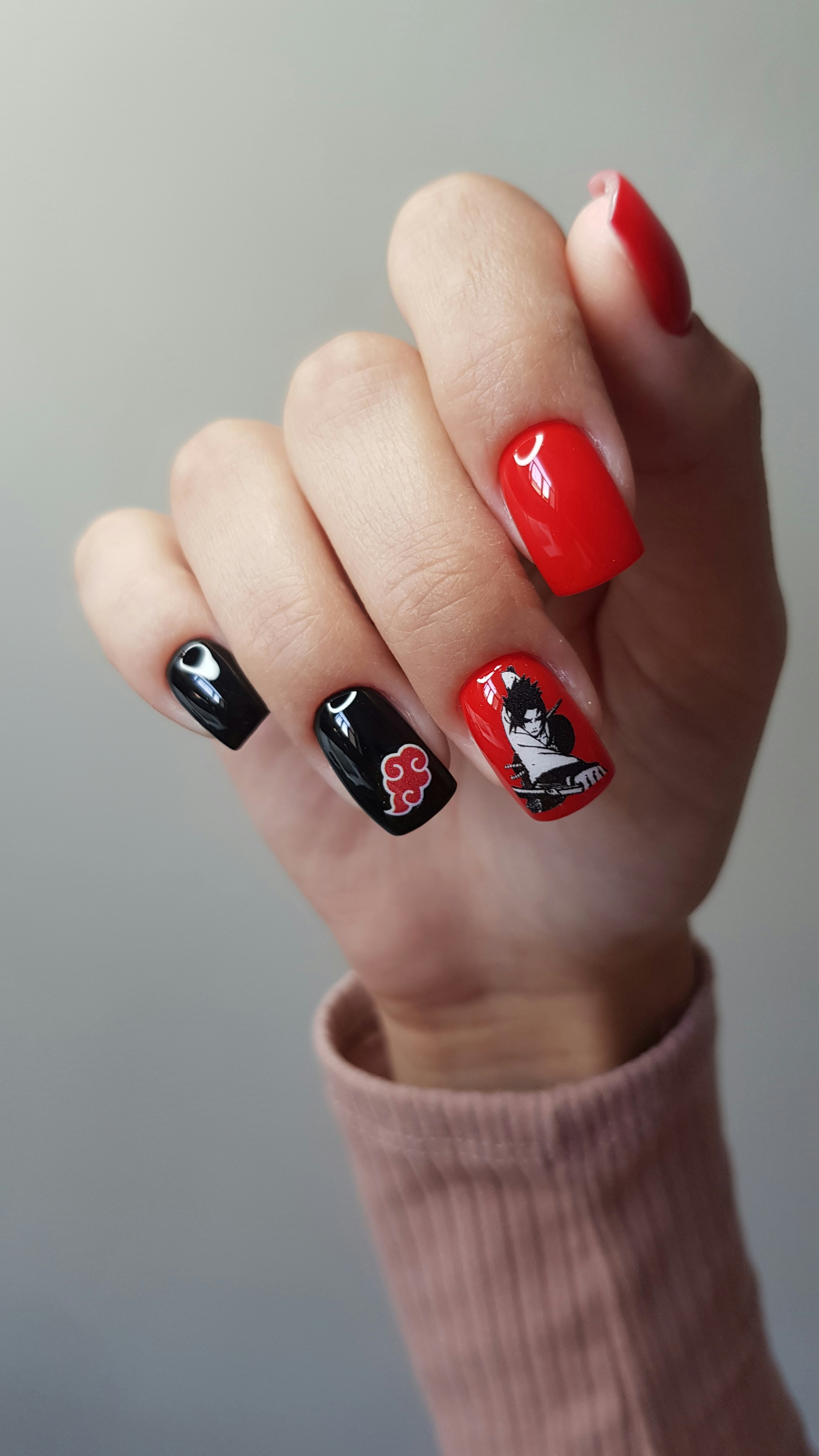 Main avec des ongles noirs et rouges mettant en scène des personnages d’anime.