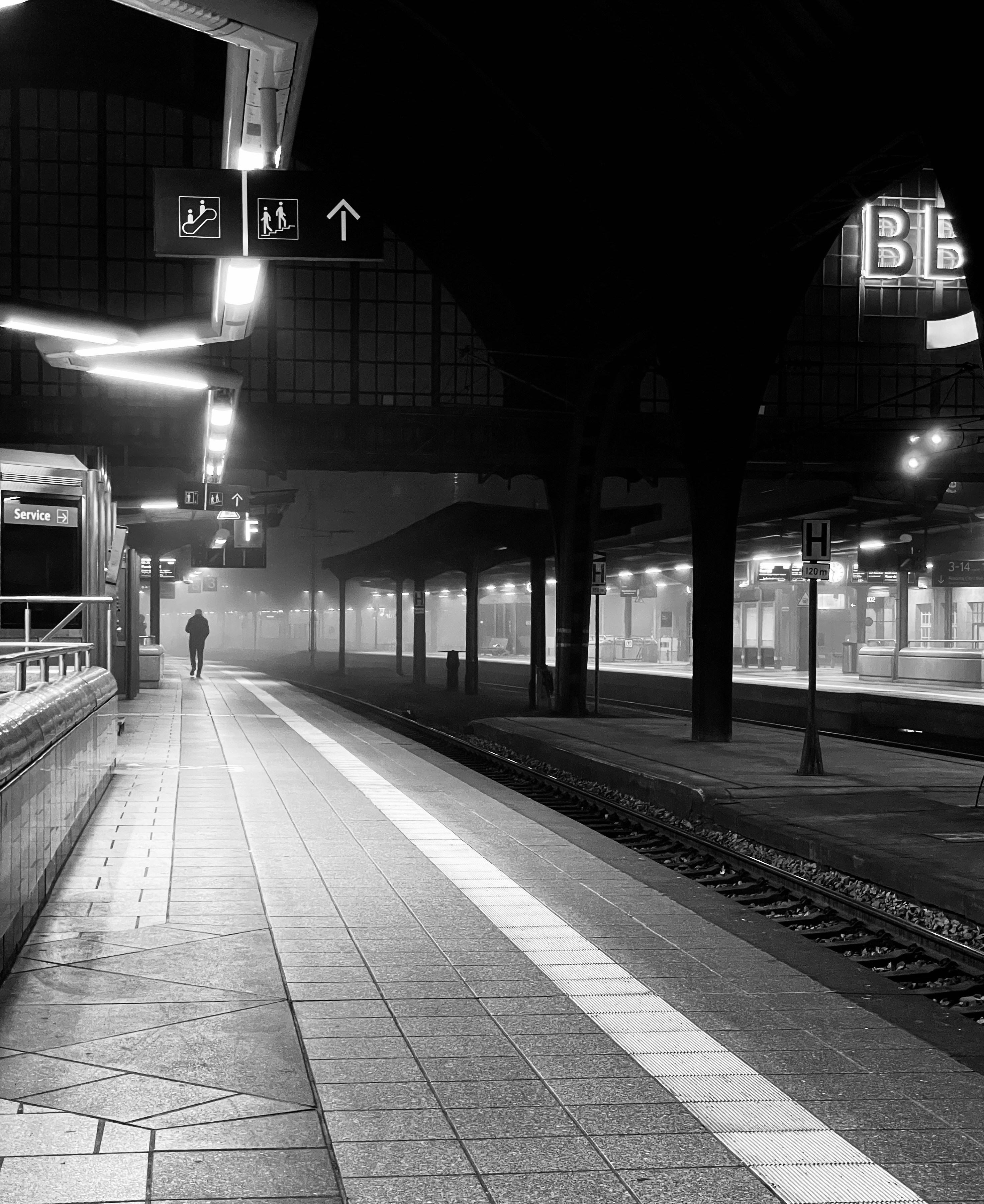 Una figura solitaria cammina lungo una banchina nebbiosa della stazione ferroviaria.