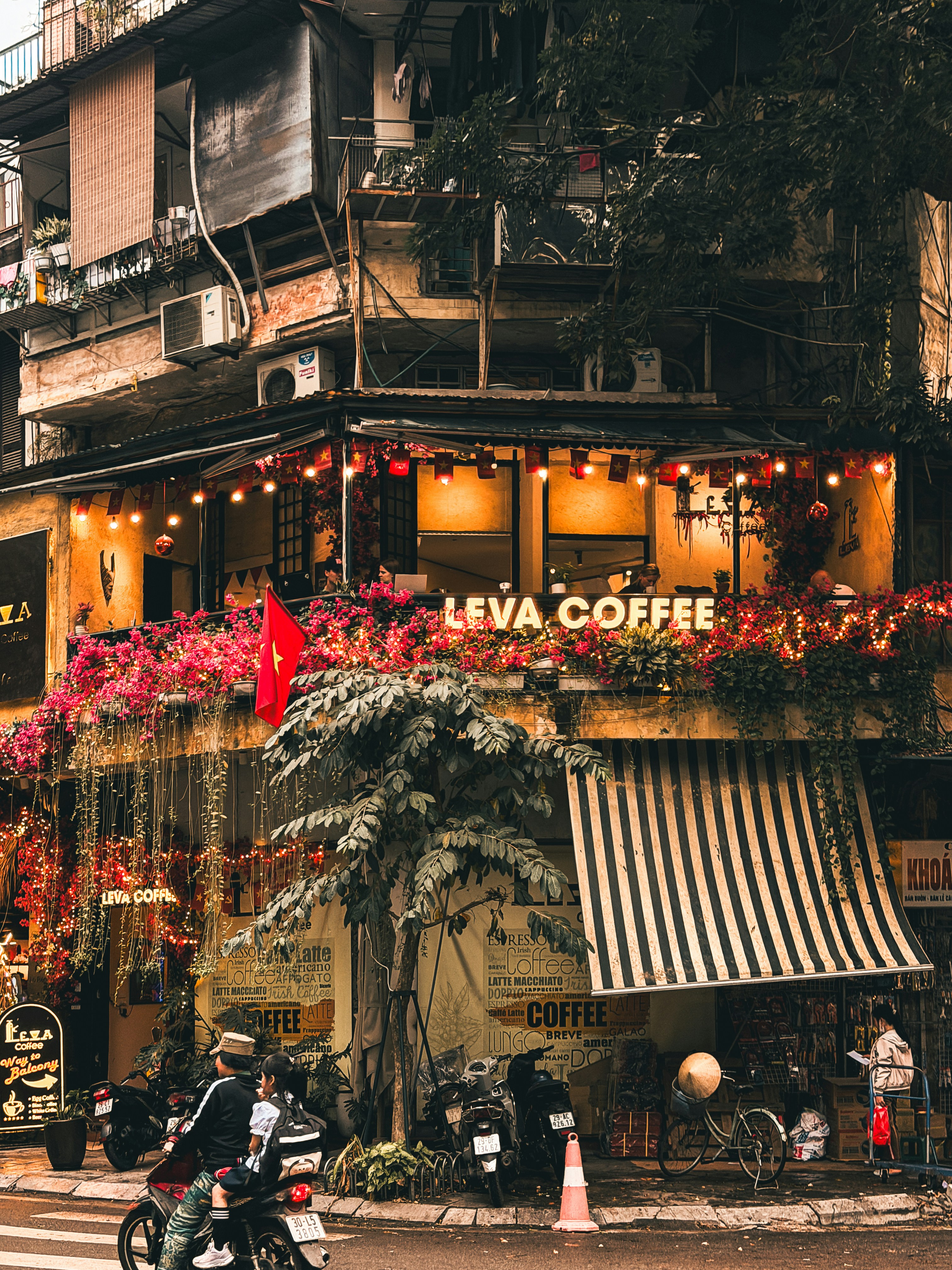 A coffee shop with flowers and lights on a street.