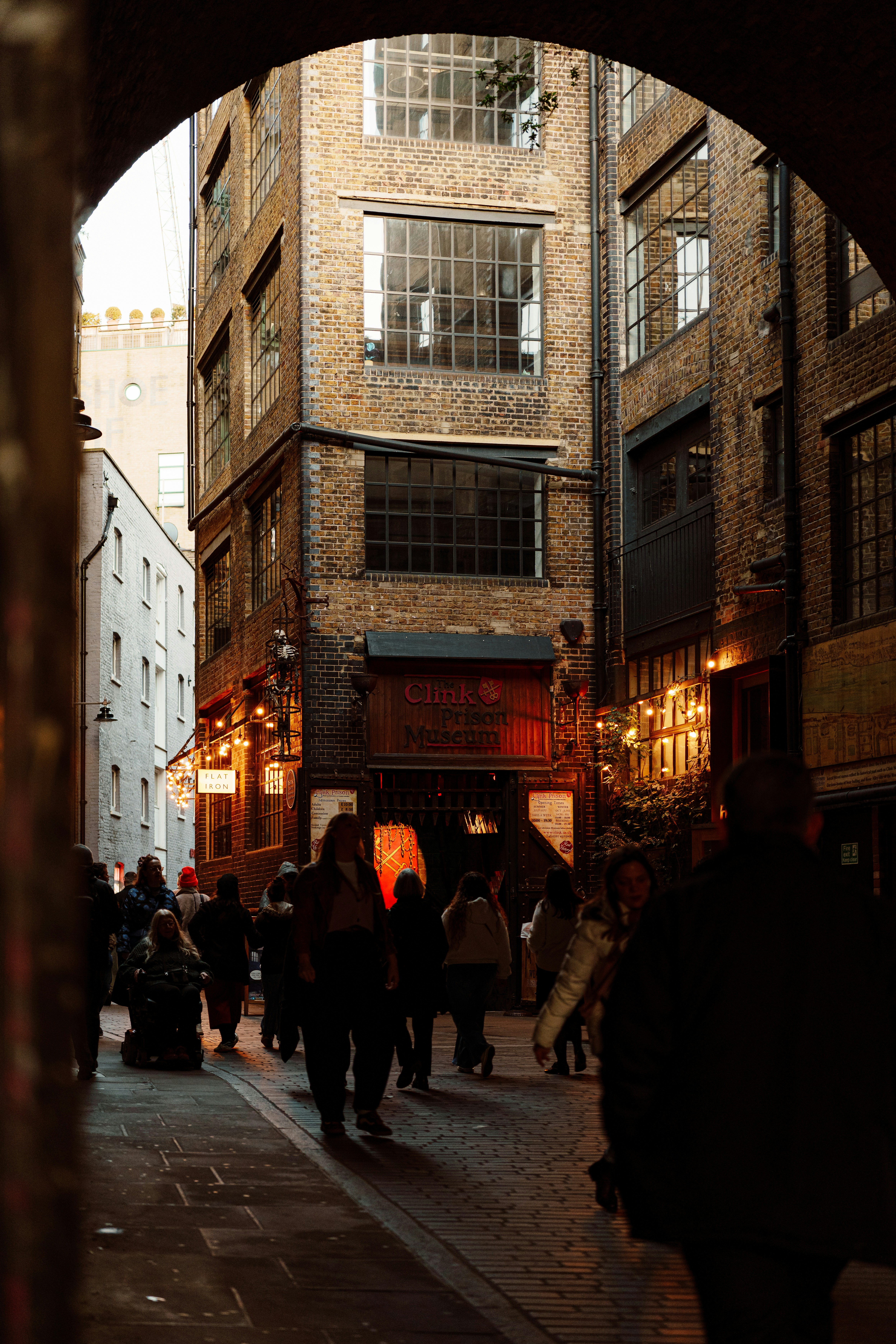 People walking down a narrow brick alleyway at dusk.