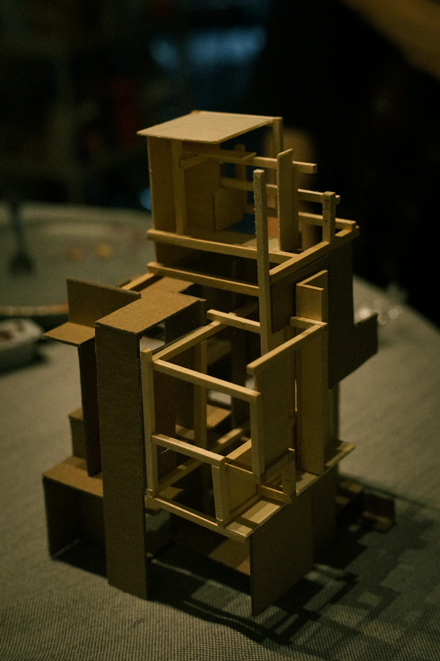 A tall study model built from brown cardboard planes and thin wood sticks, standing on a table