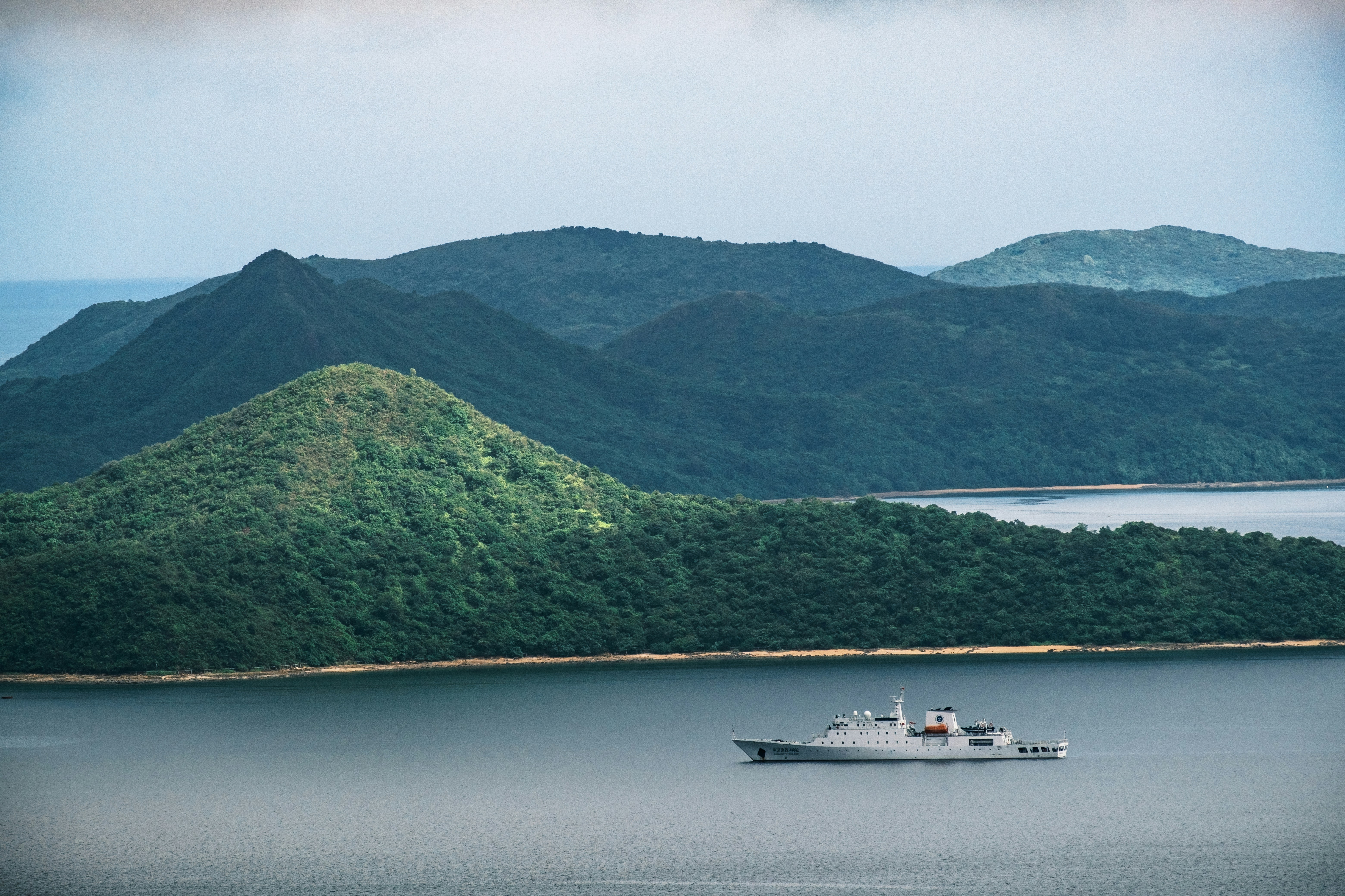現代の軍艦は森林に覆われた島々の穏やかな水面を航行しています。