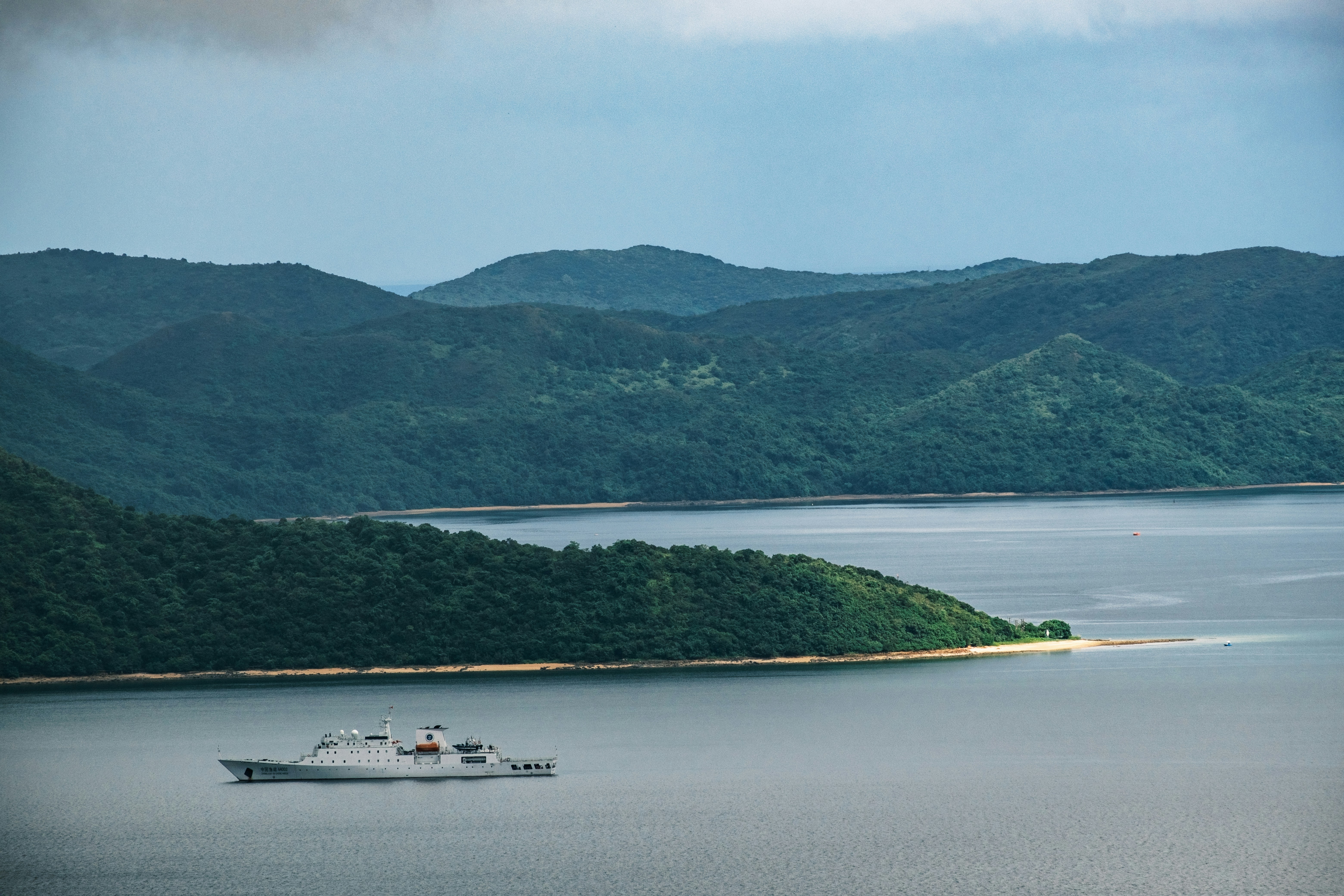 現代の船が緑の丘の近くの水上を航行しています。
