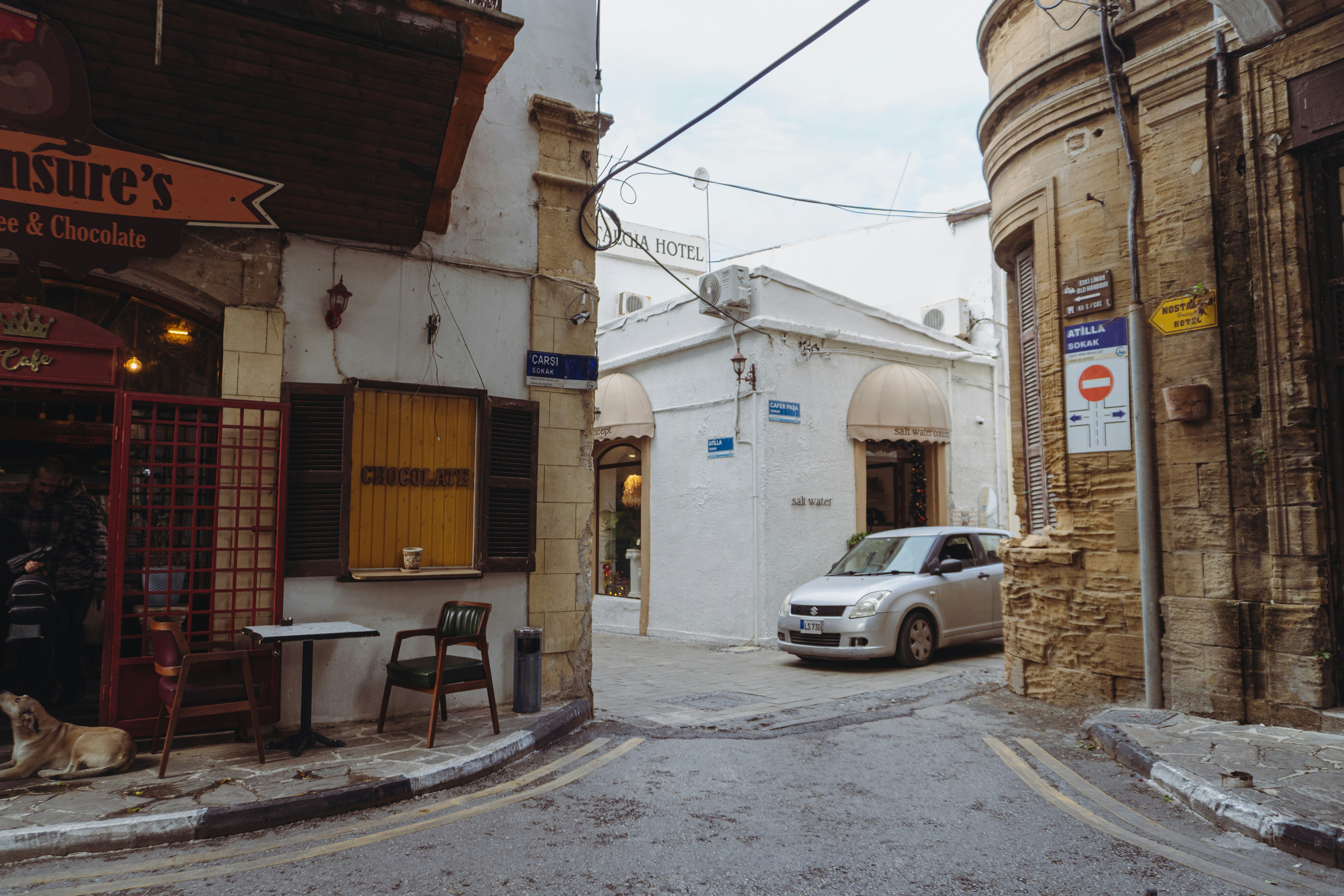A silver car drives down a narrow european street.
