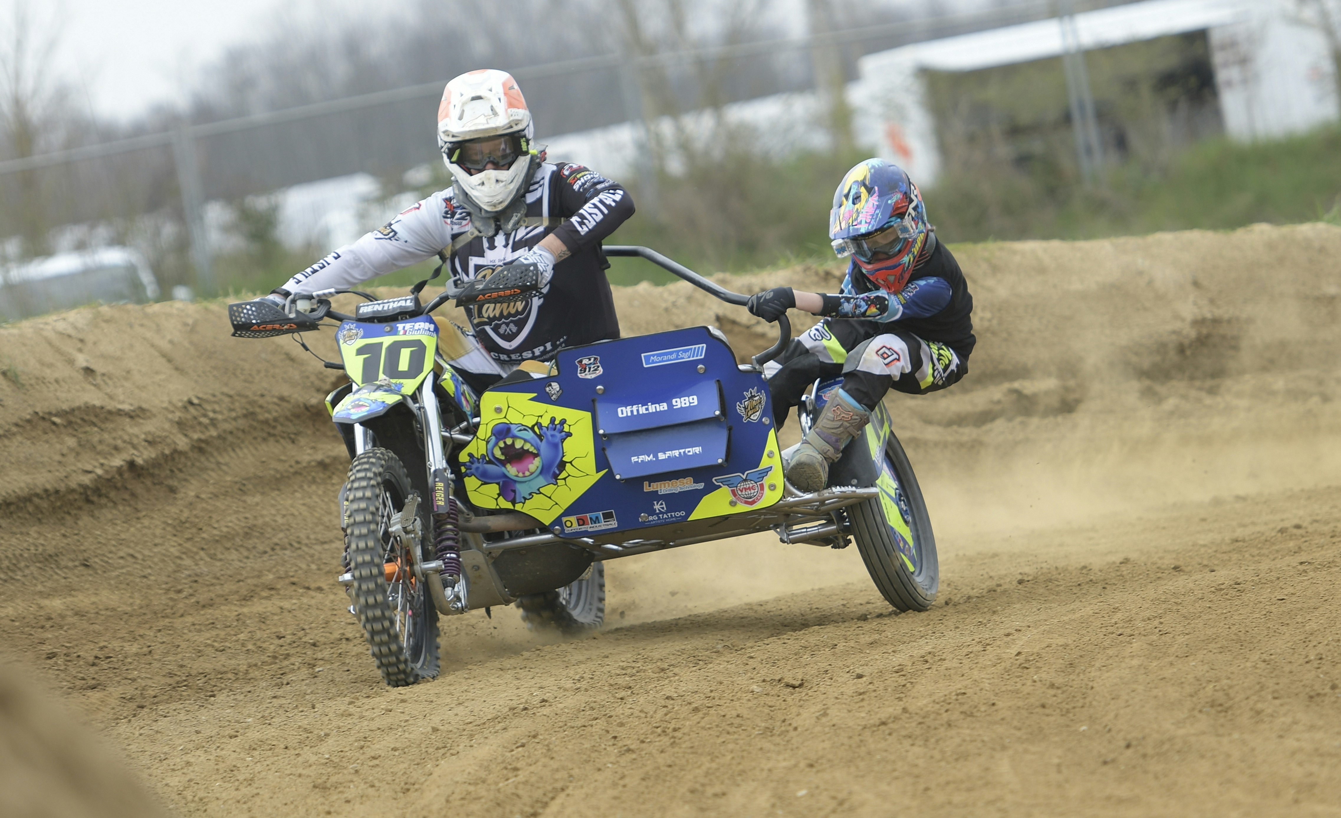 Two people riding a sidecar motorcycle on a dirt track