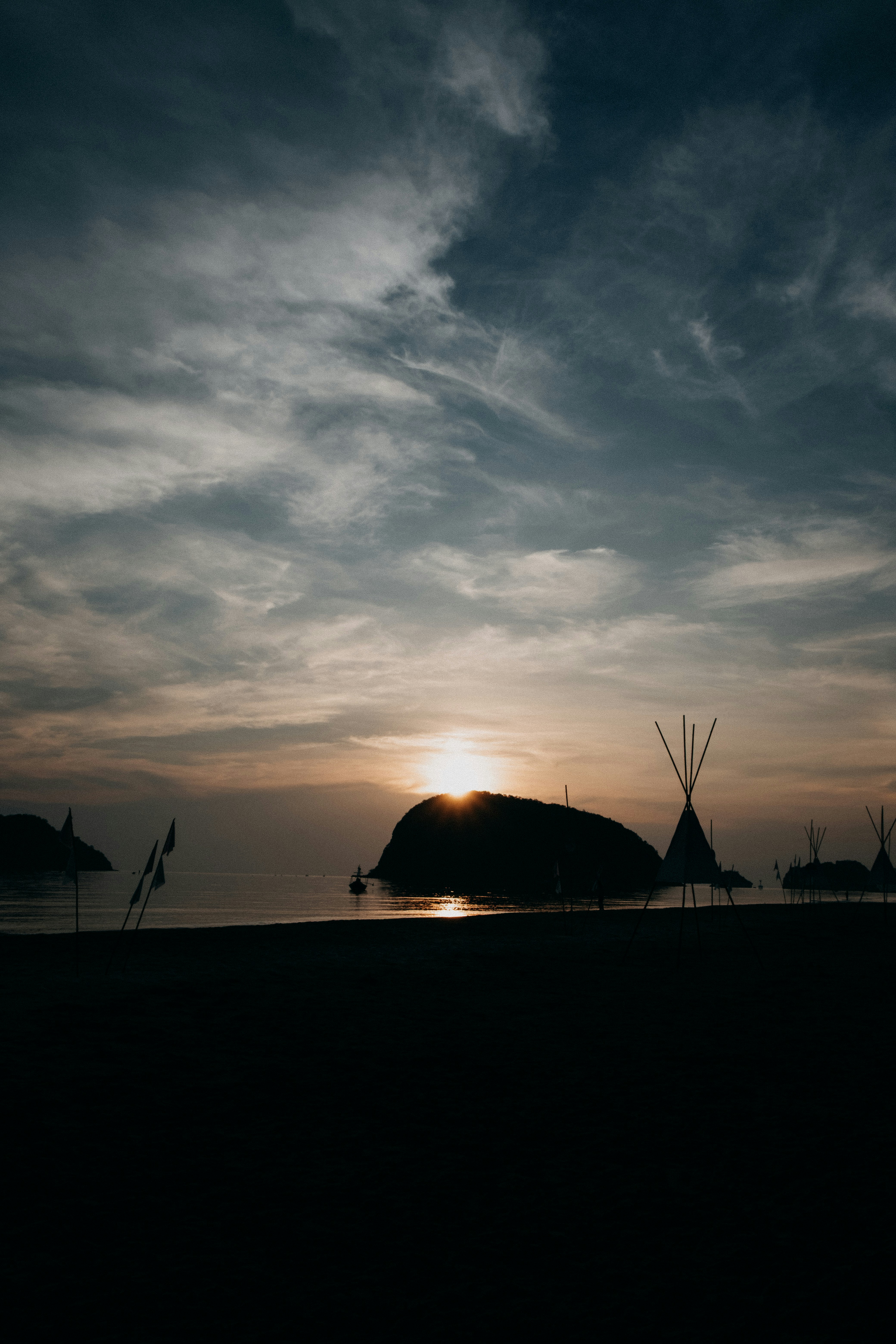 Sunset over a calm ocean with silhouetted tents.