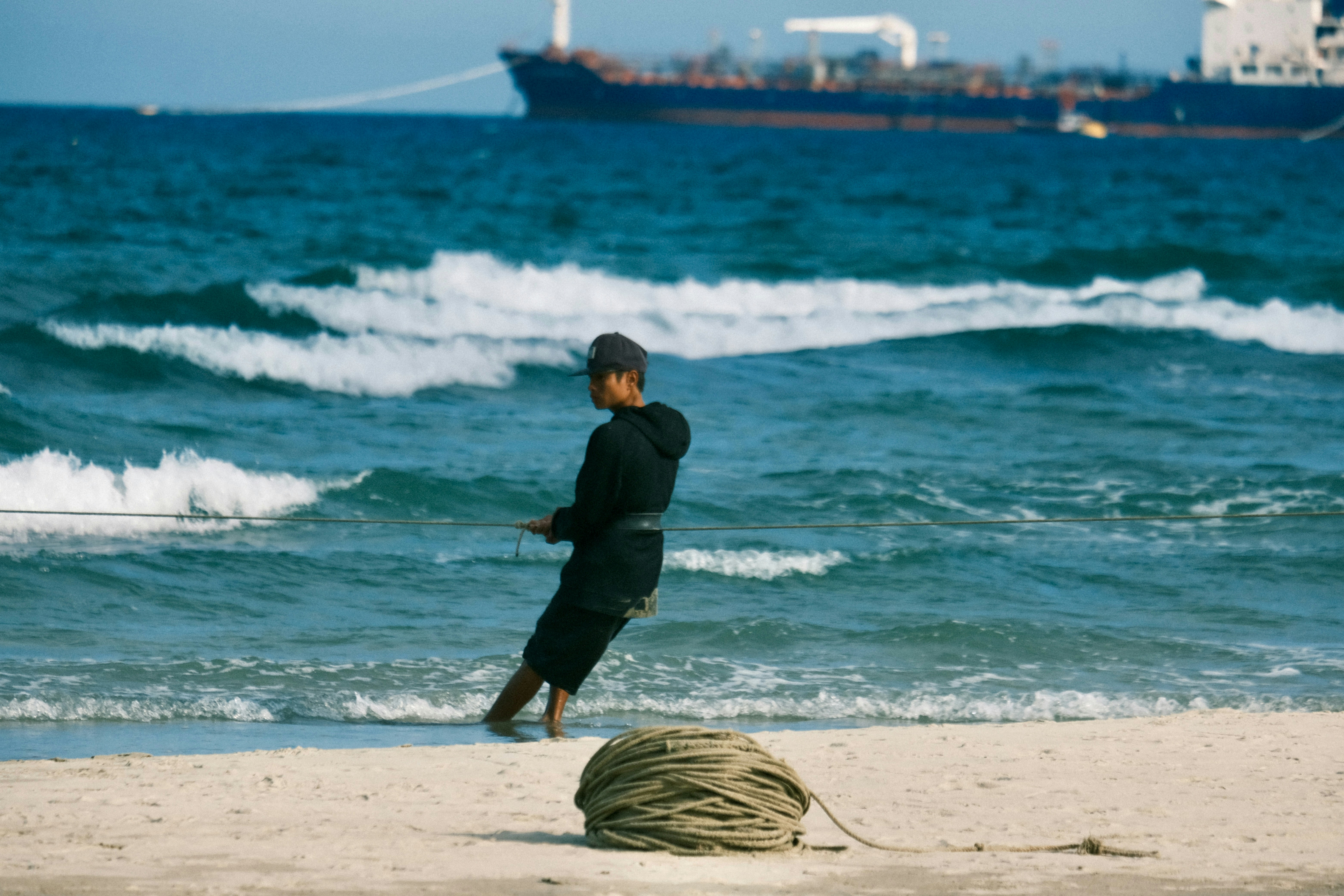 Uomo che tira la corda sulla spiaggia con nave al largo