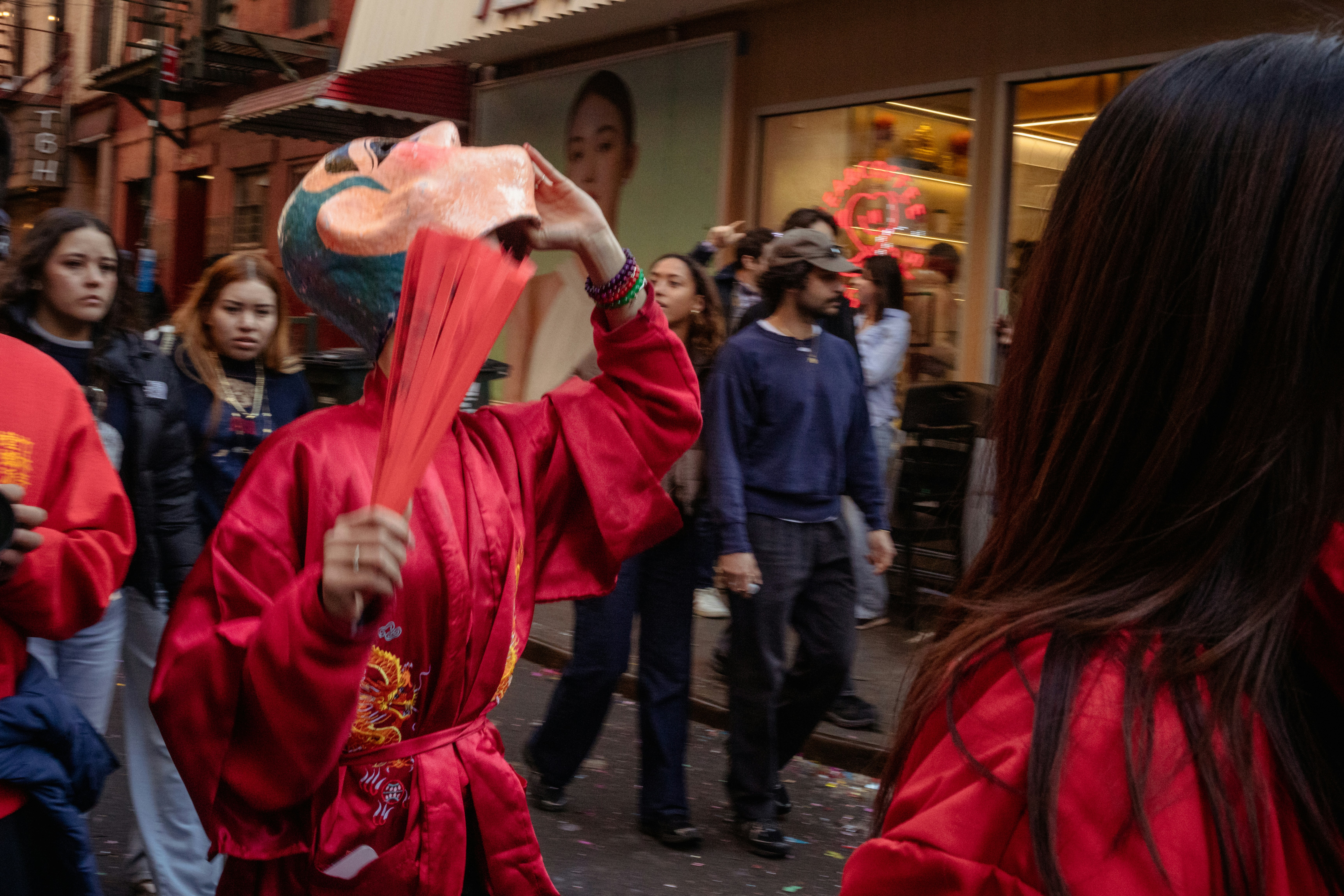 Person in red robe holds fan and mask at festival.
