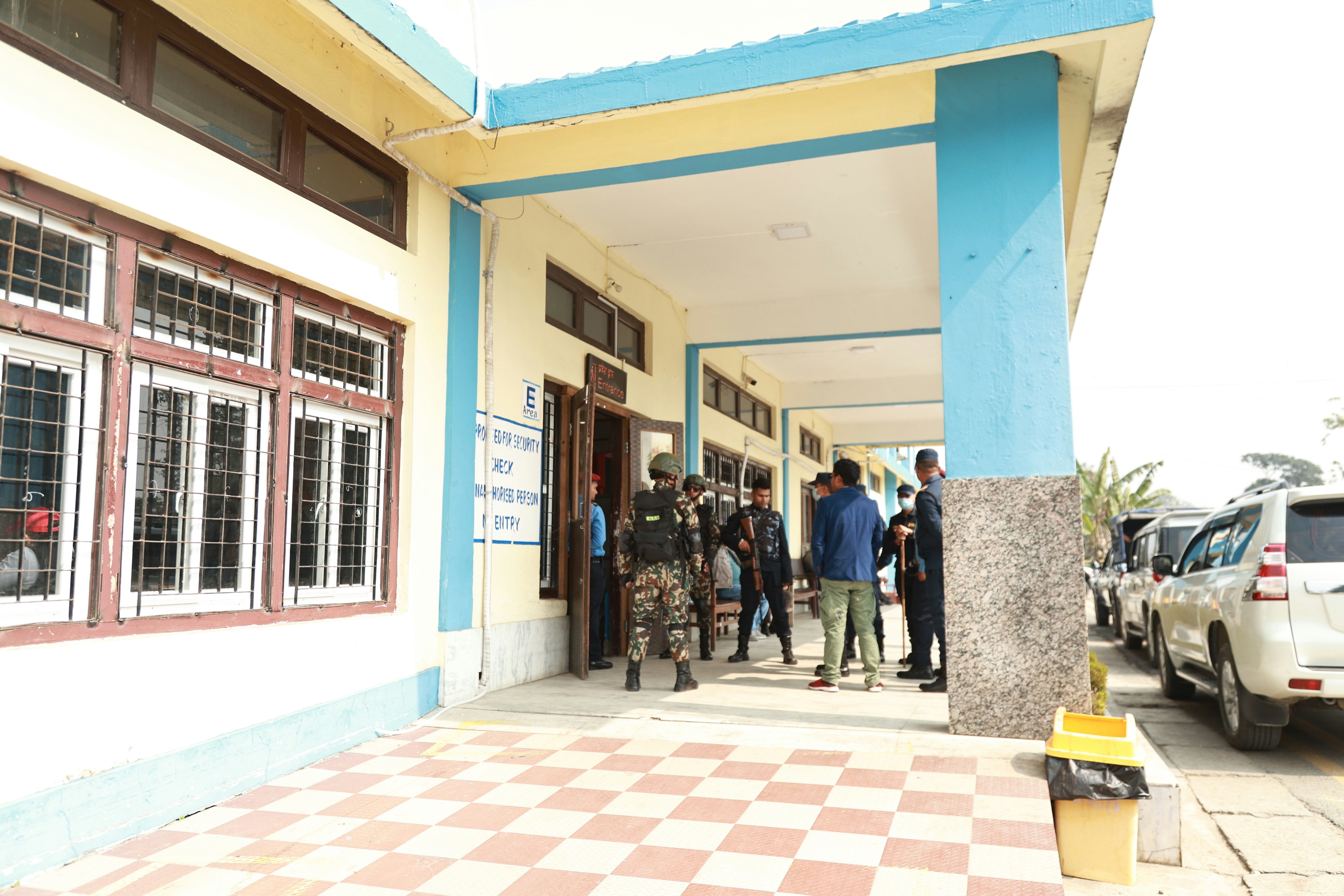 People gathered outside a building entrance with parked vehicles.