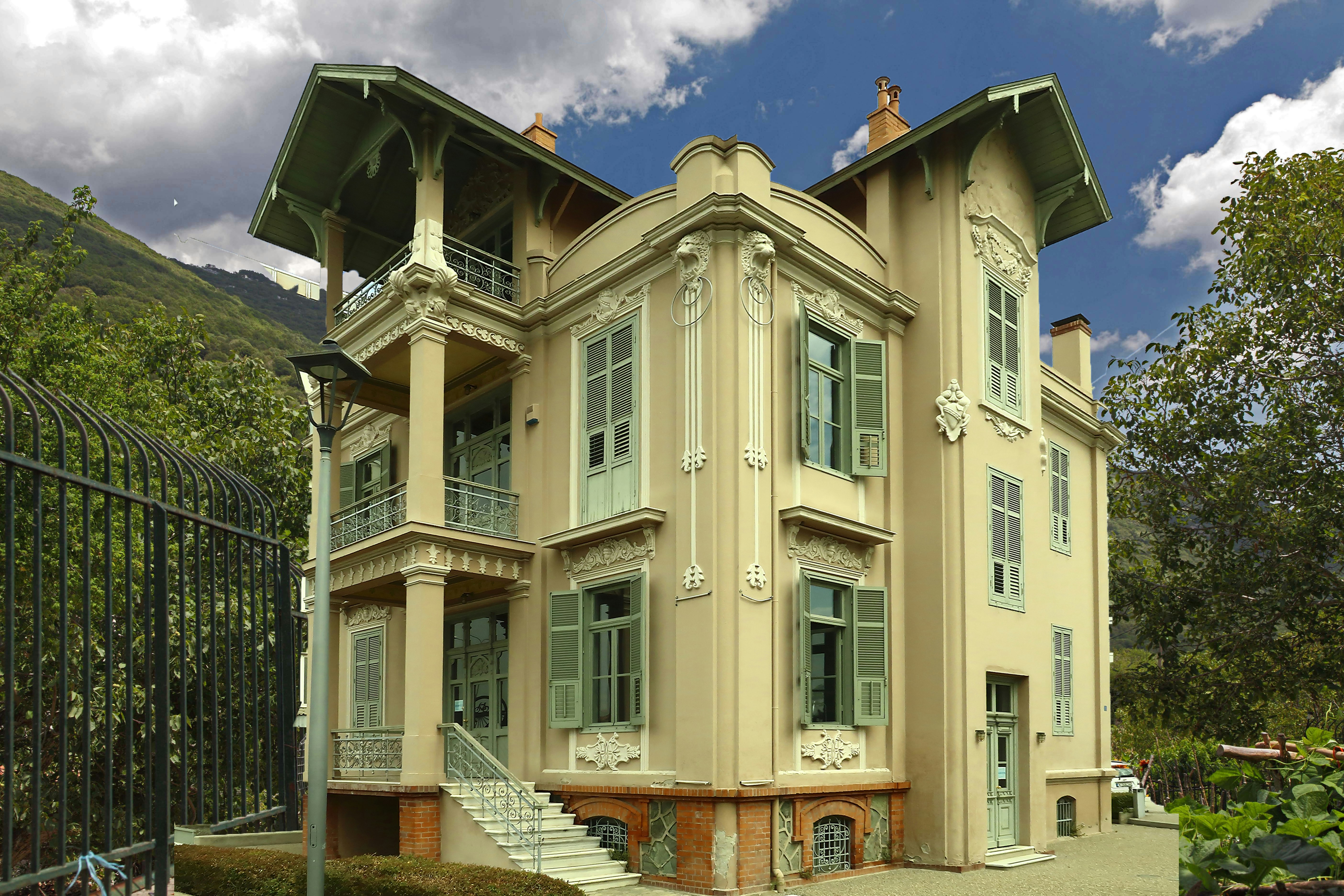 A large, ornate beige house with green shutters.