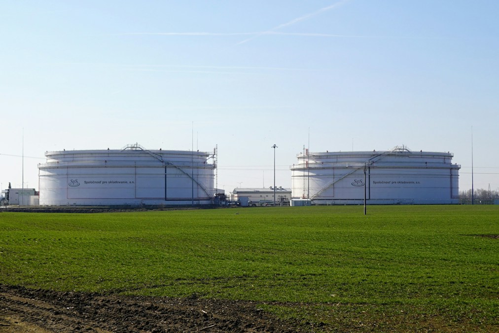 Deux grands réservoirs blancs de stockage de carburant au bord d’un champ, sous un ciel bleu