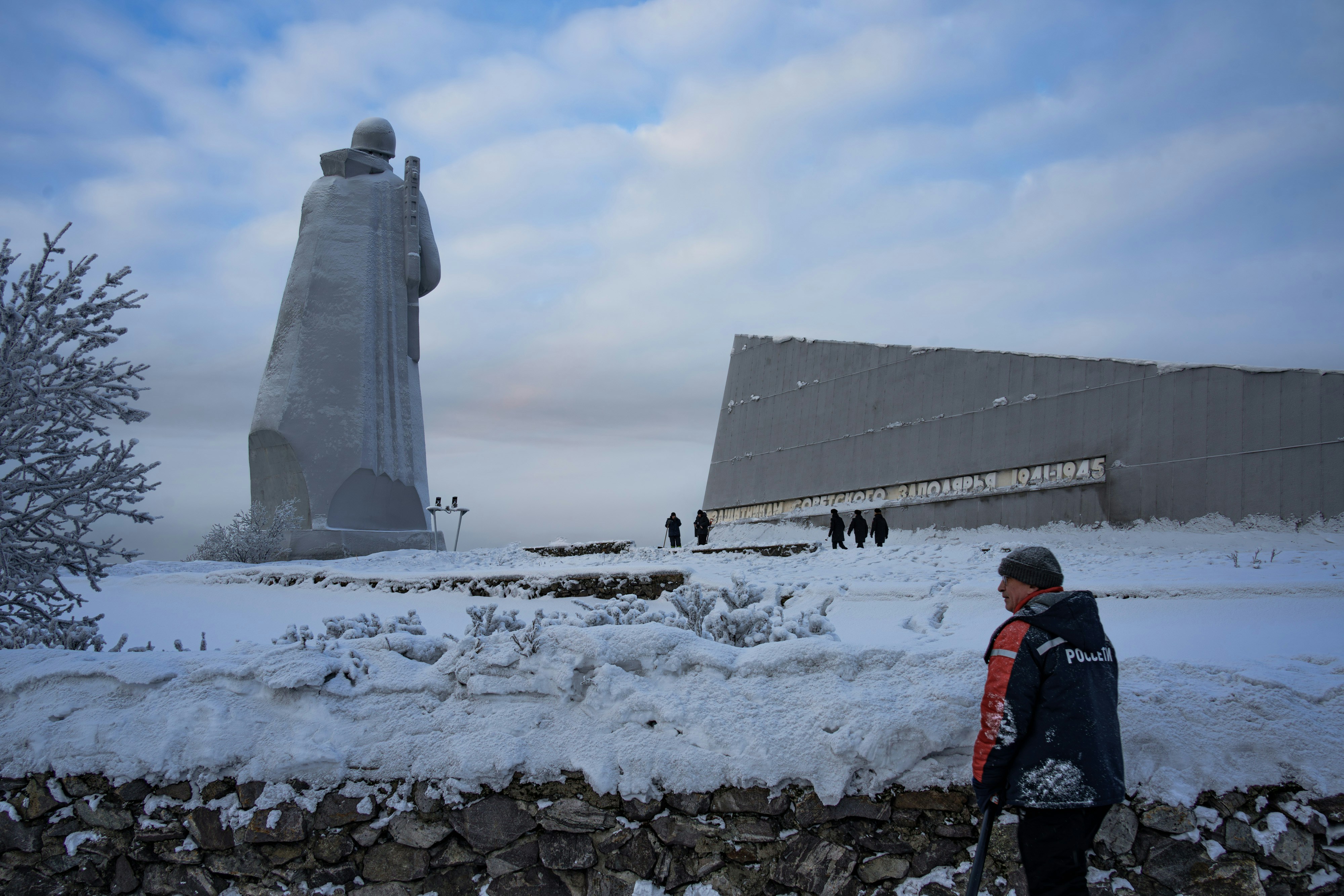 A lone figure stands before a large monument in snow.