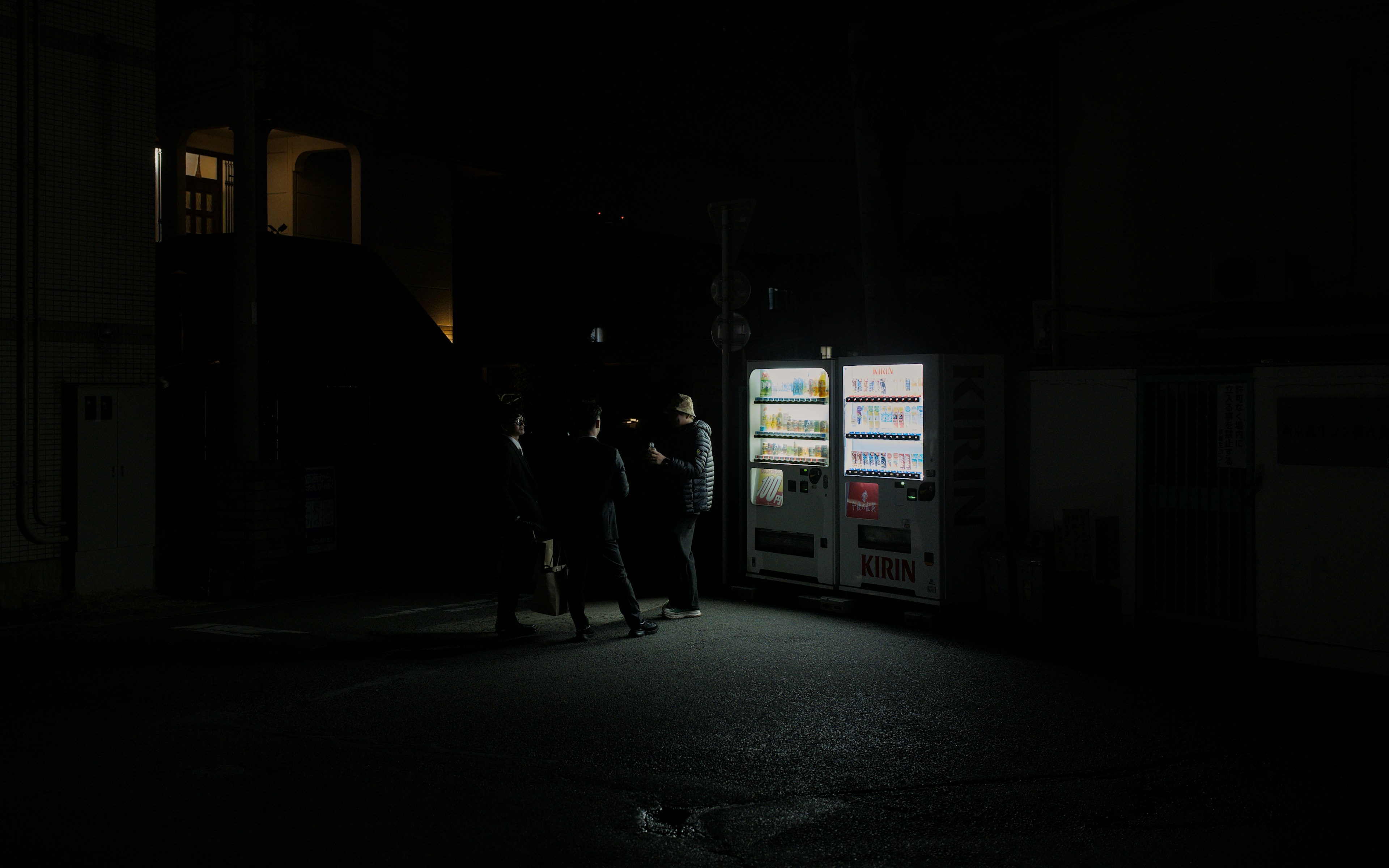 Three figures stand by a lit vending machine at night.
