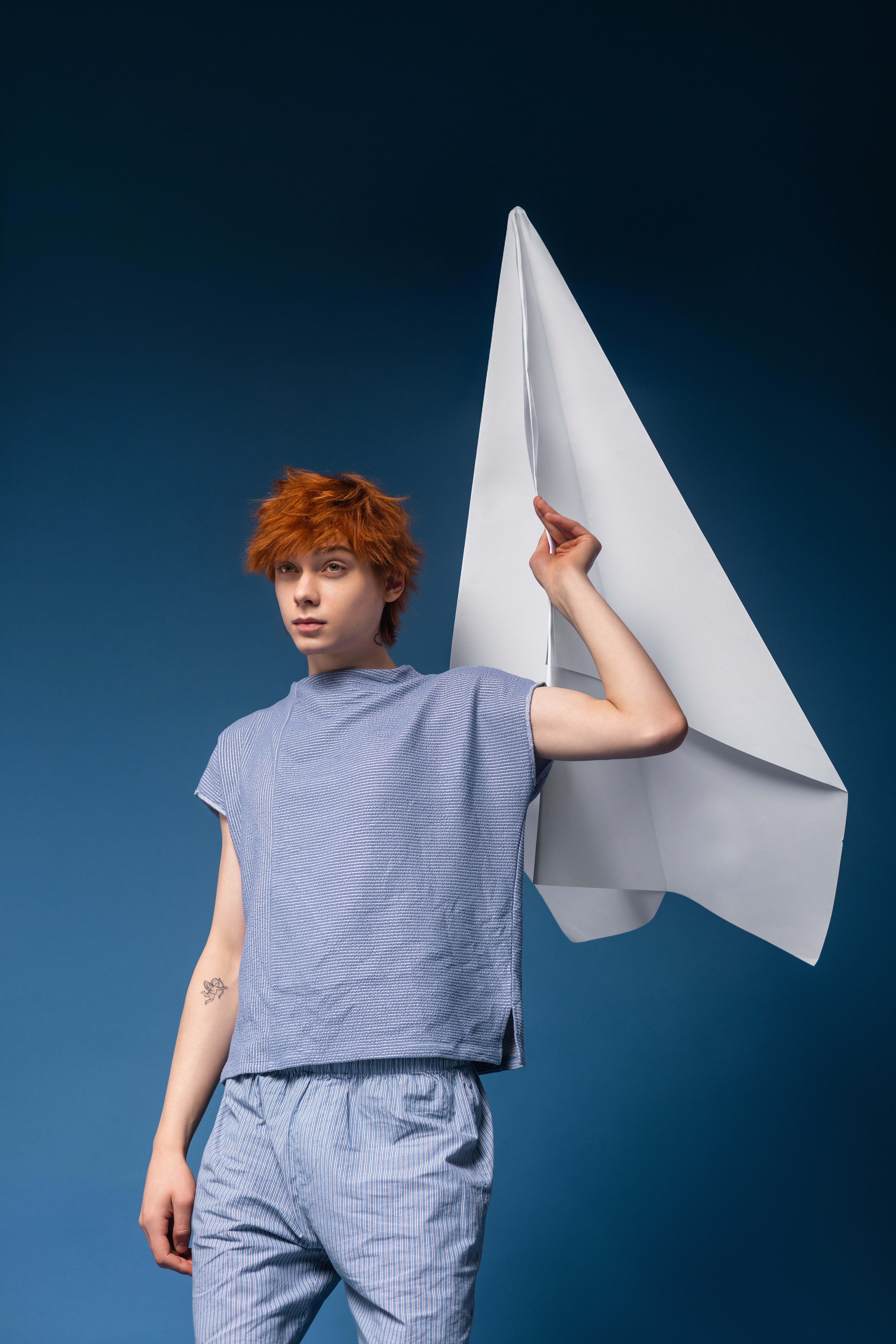 Young person with red hair holding a large paper airplane