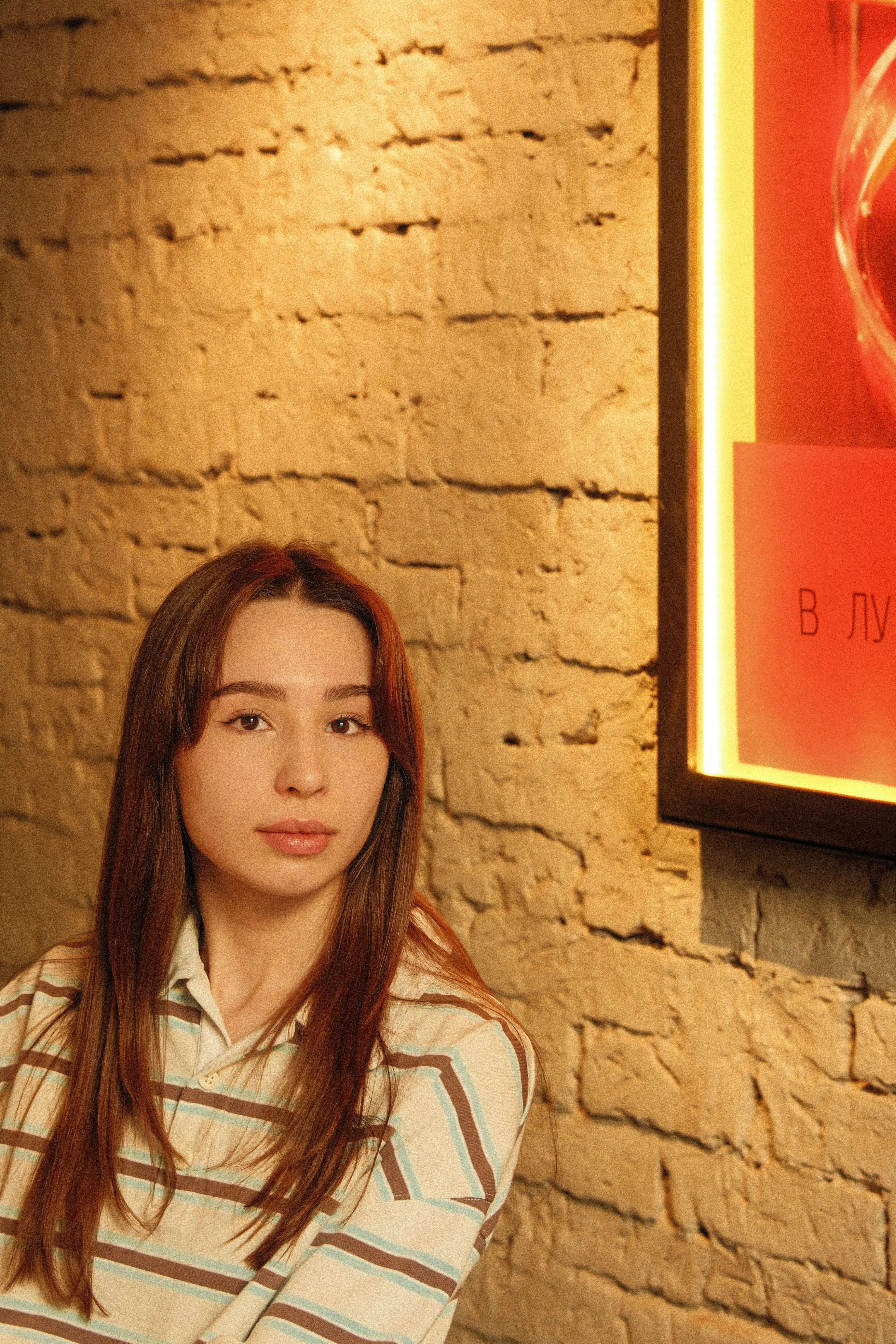 Young woman with long brown hair by brick wall
