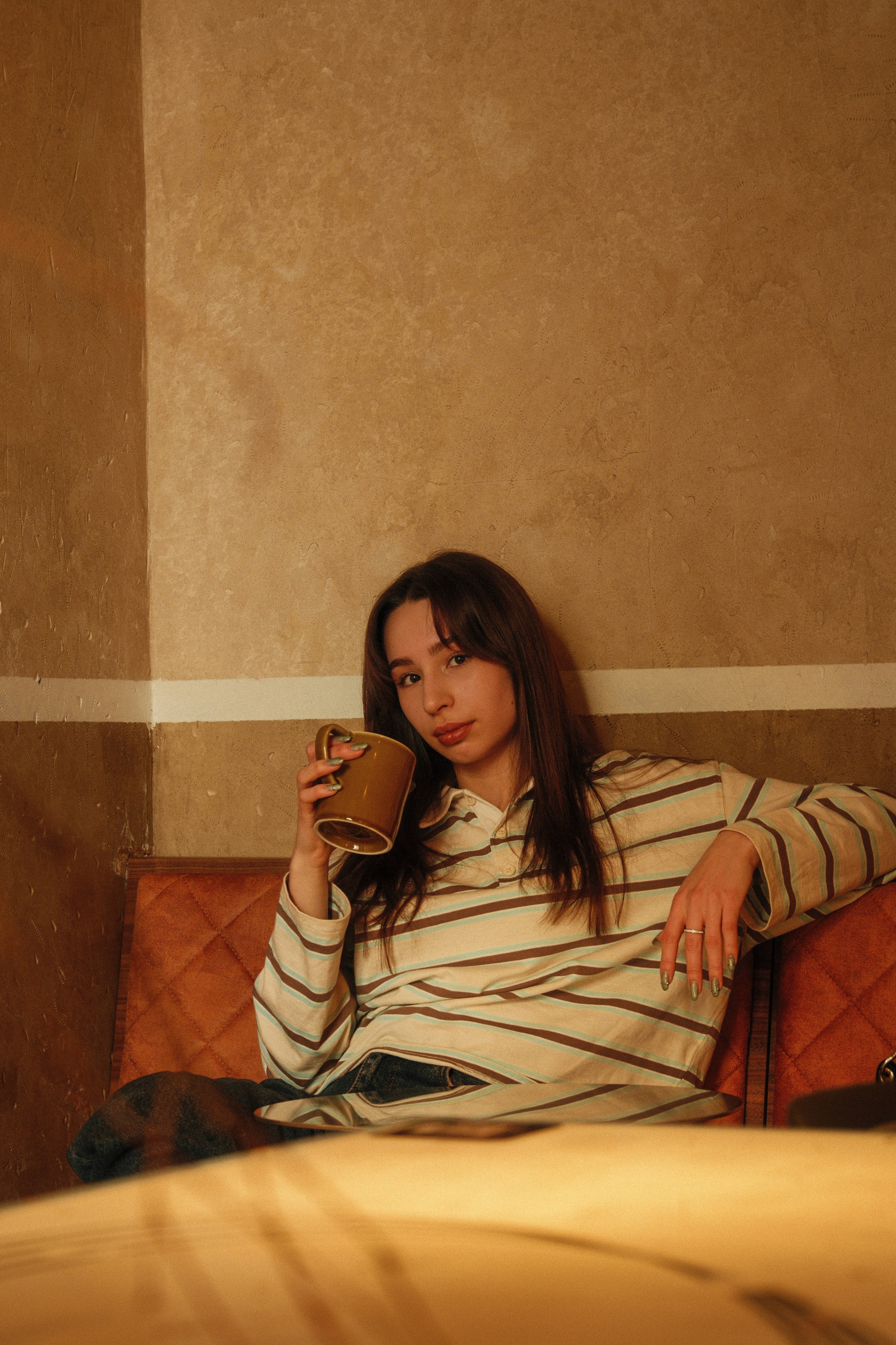 A young woman drinks from a mug on a couch.