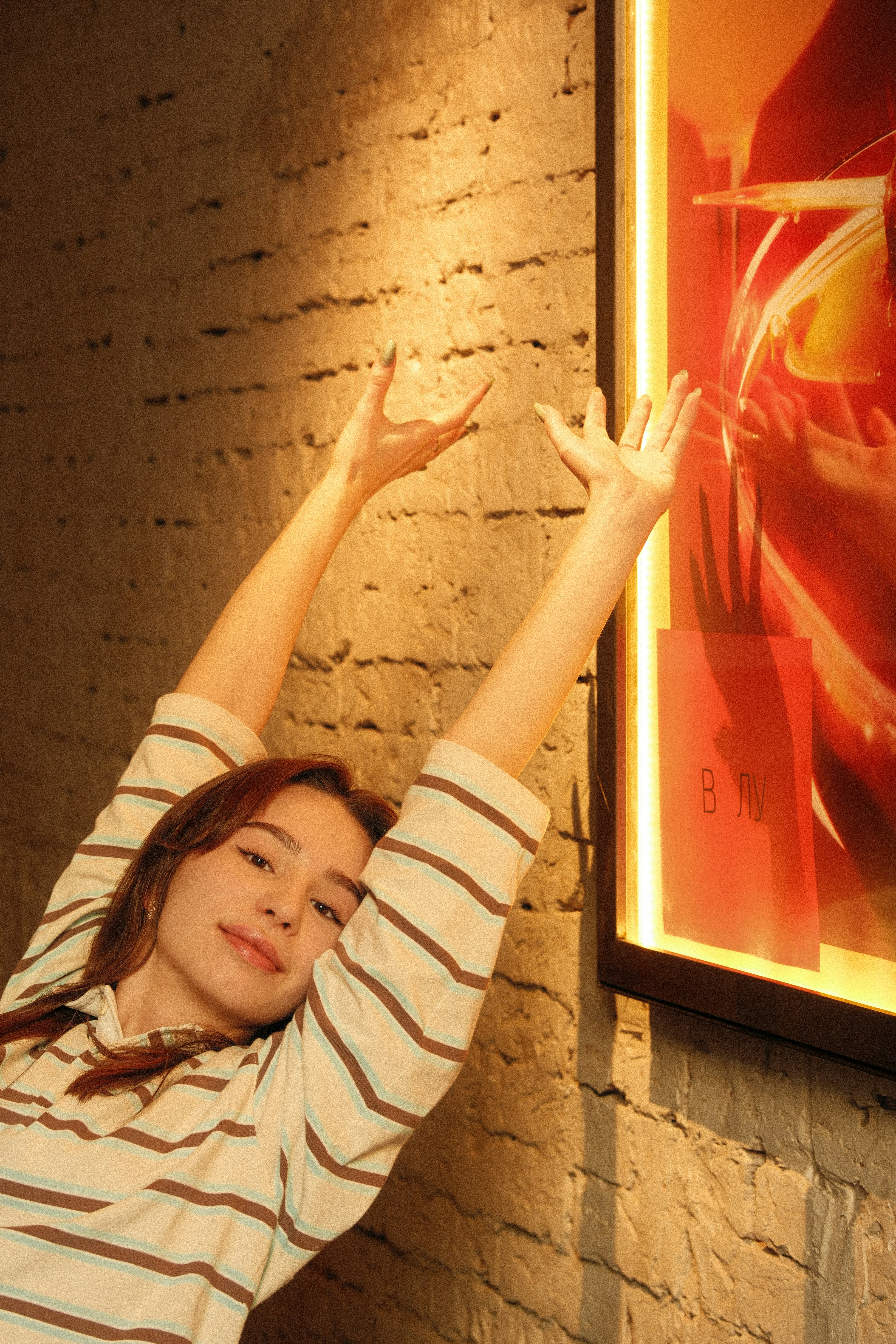 A young woman stretches her arms up near a wall.