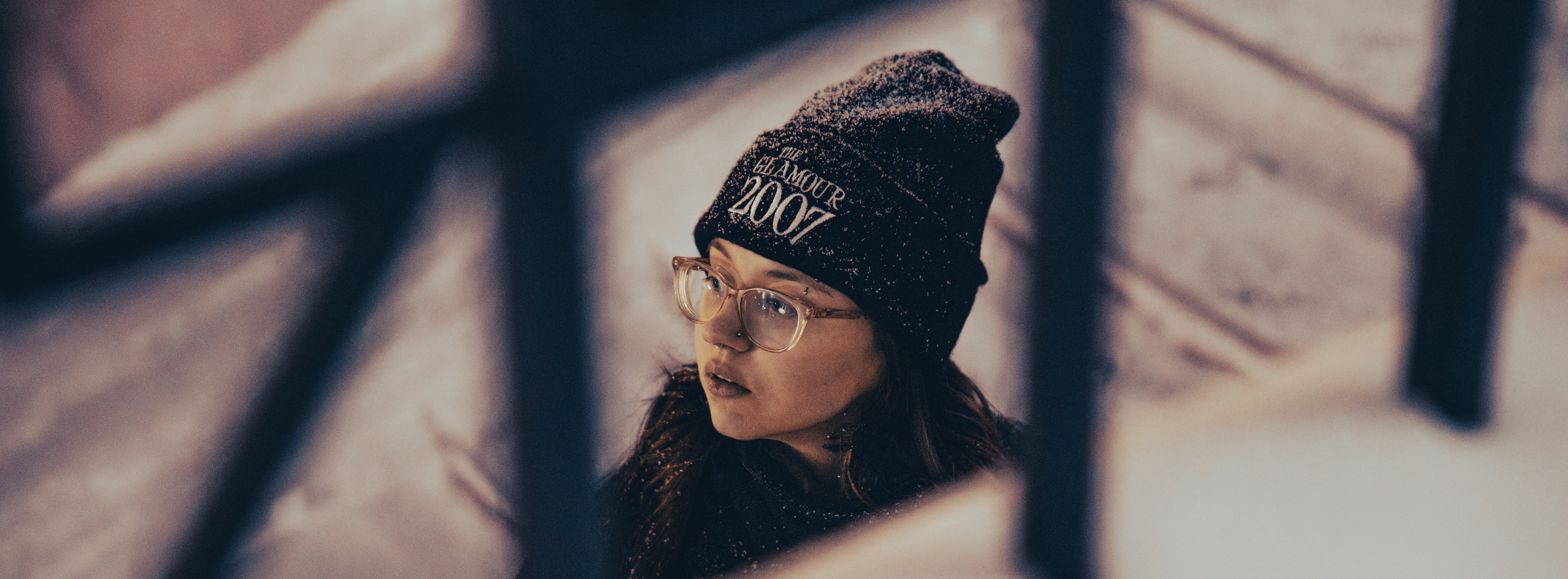 Young woman wearing glasses and a beanie looks away.