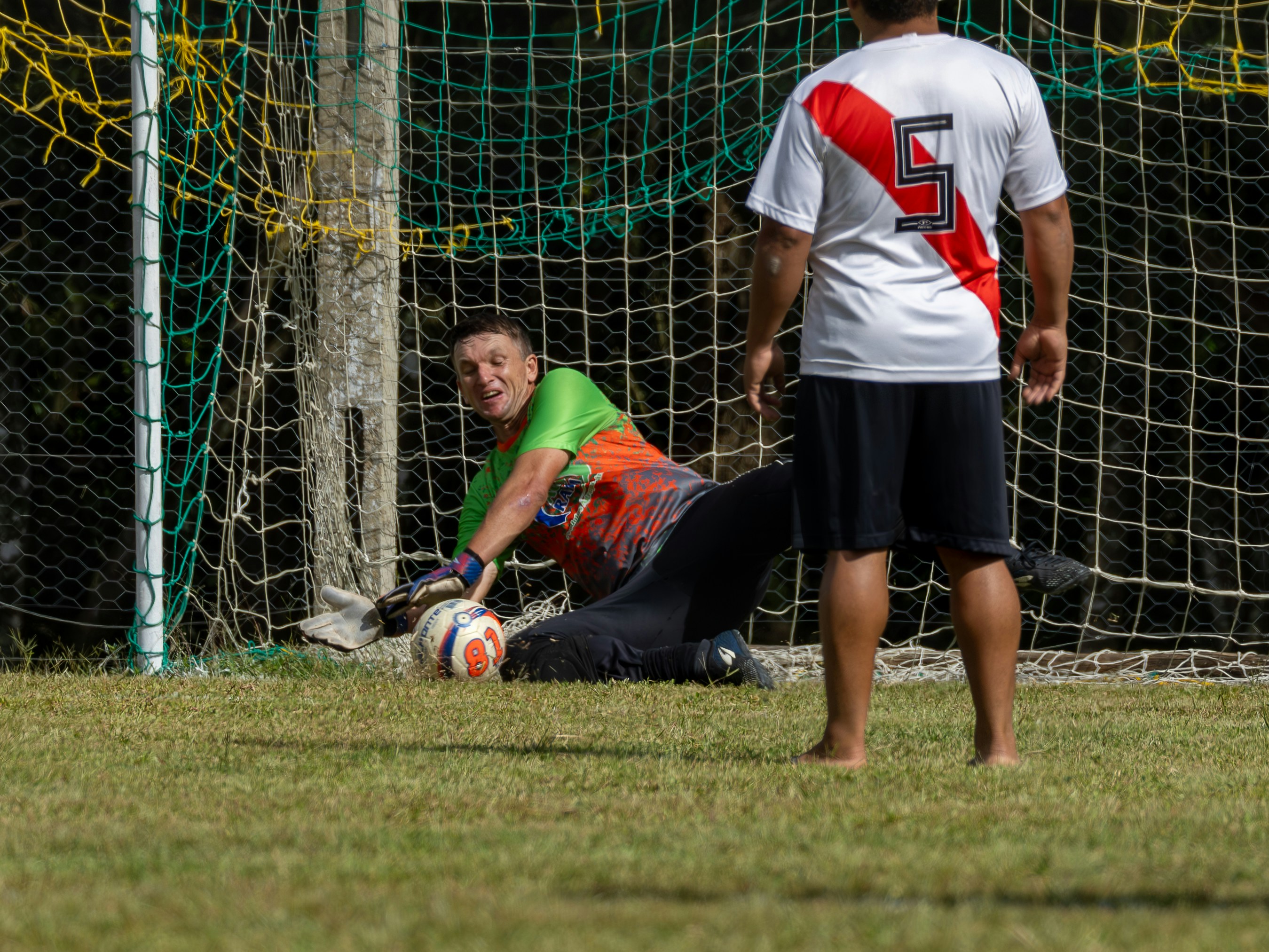Goalkeeper dives to save a soccer ball near the net.