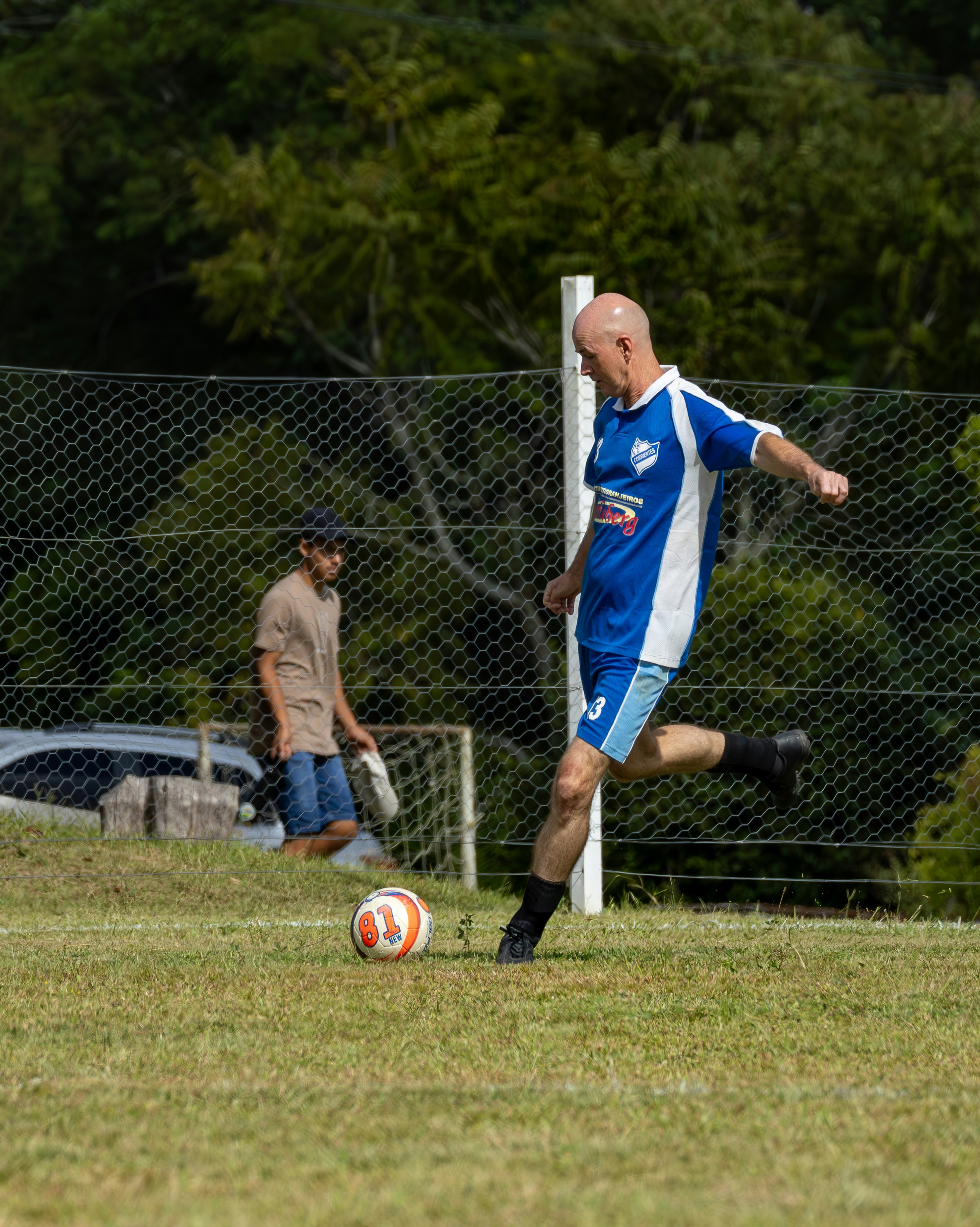 Man in blue jersey kicks soccer ball on grassy field