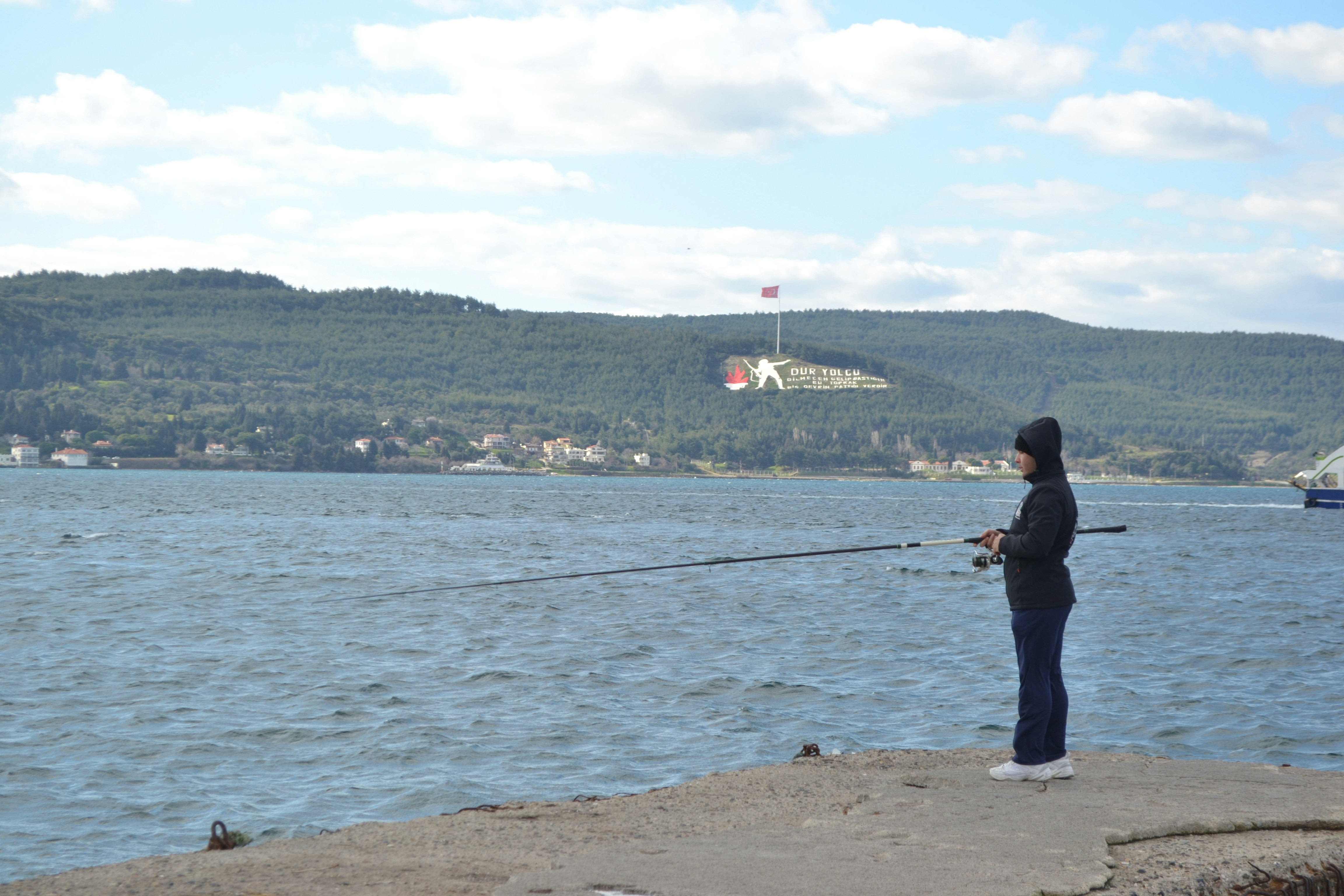 Person fishing by the water with hills in background.