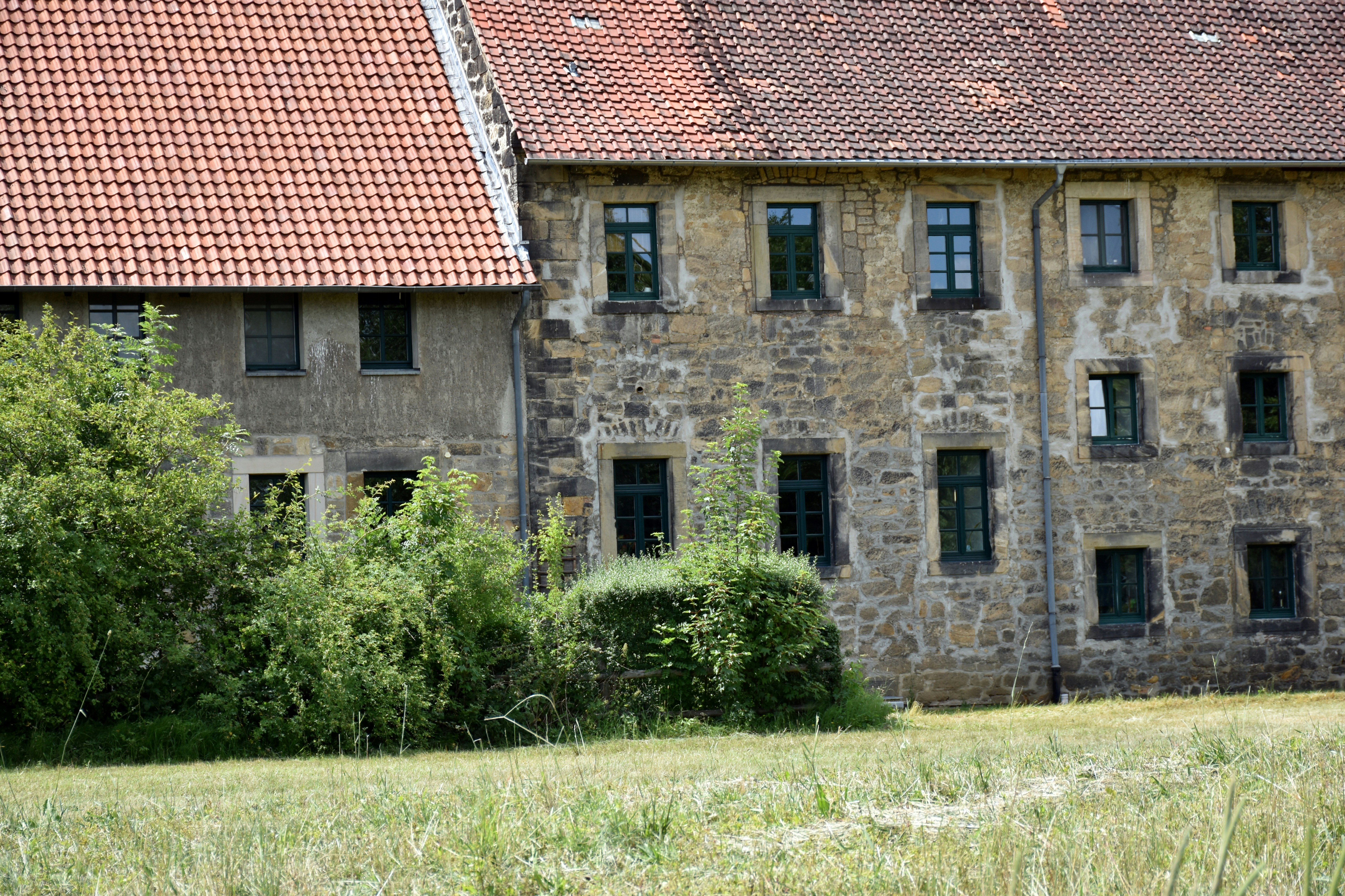 Old stone building with red tiled roof and greenery