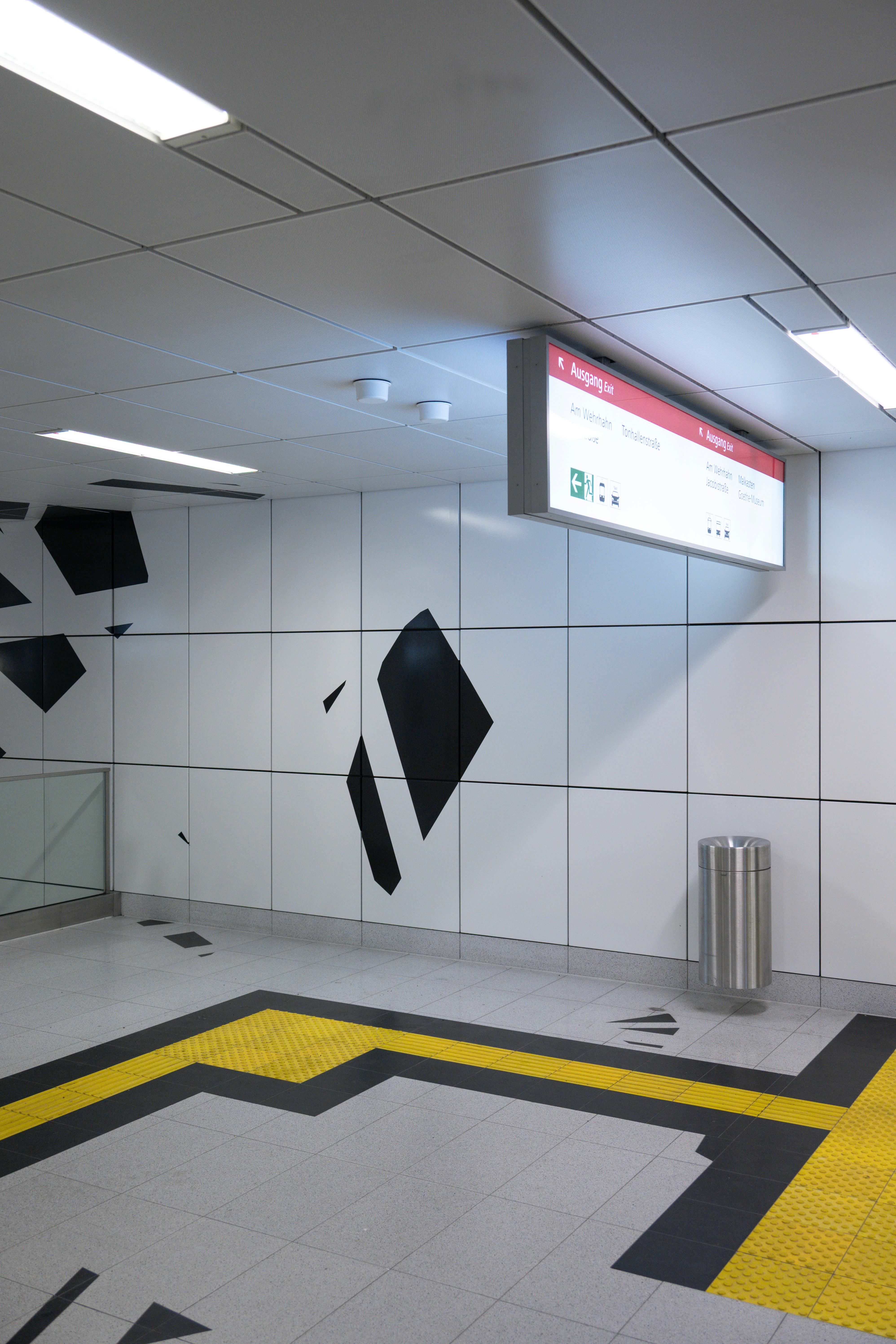 Intérieur moderne de station de métro avec signalétique et pavage tactile jaune.