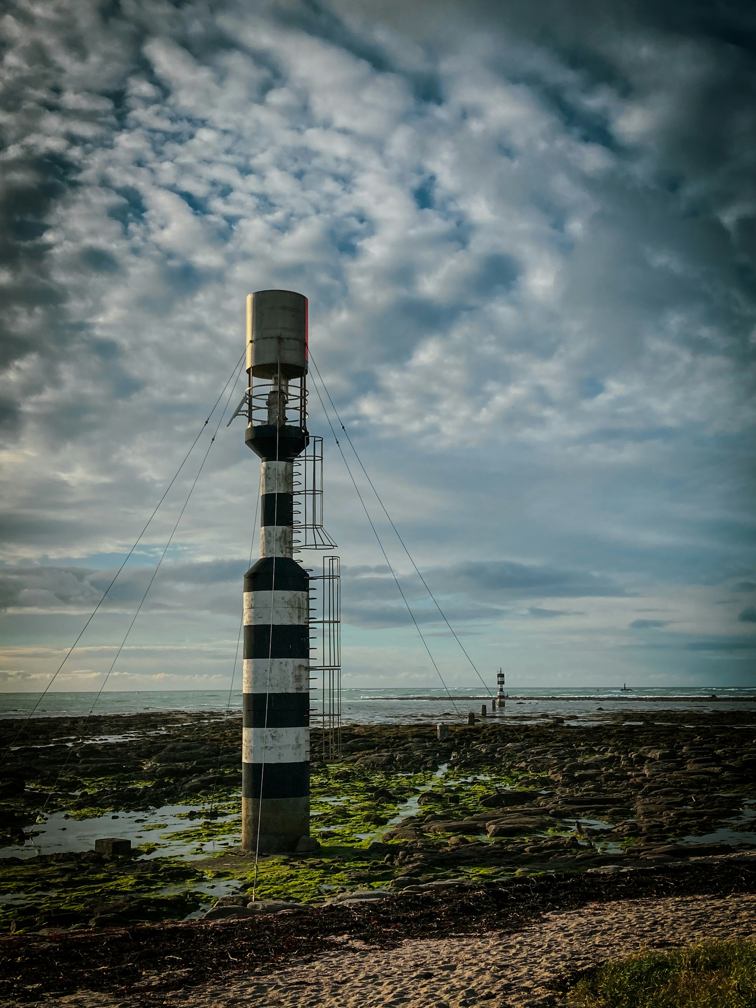 Striped lighthouse on a rocky shore under cloudy sky