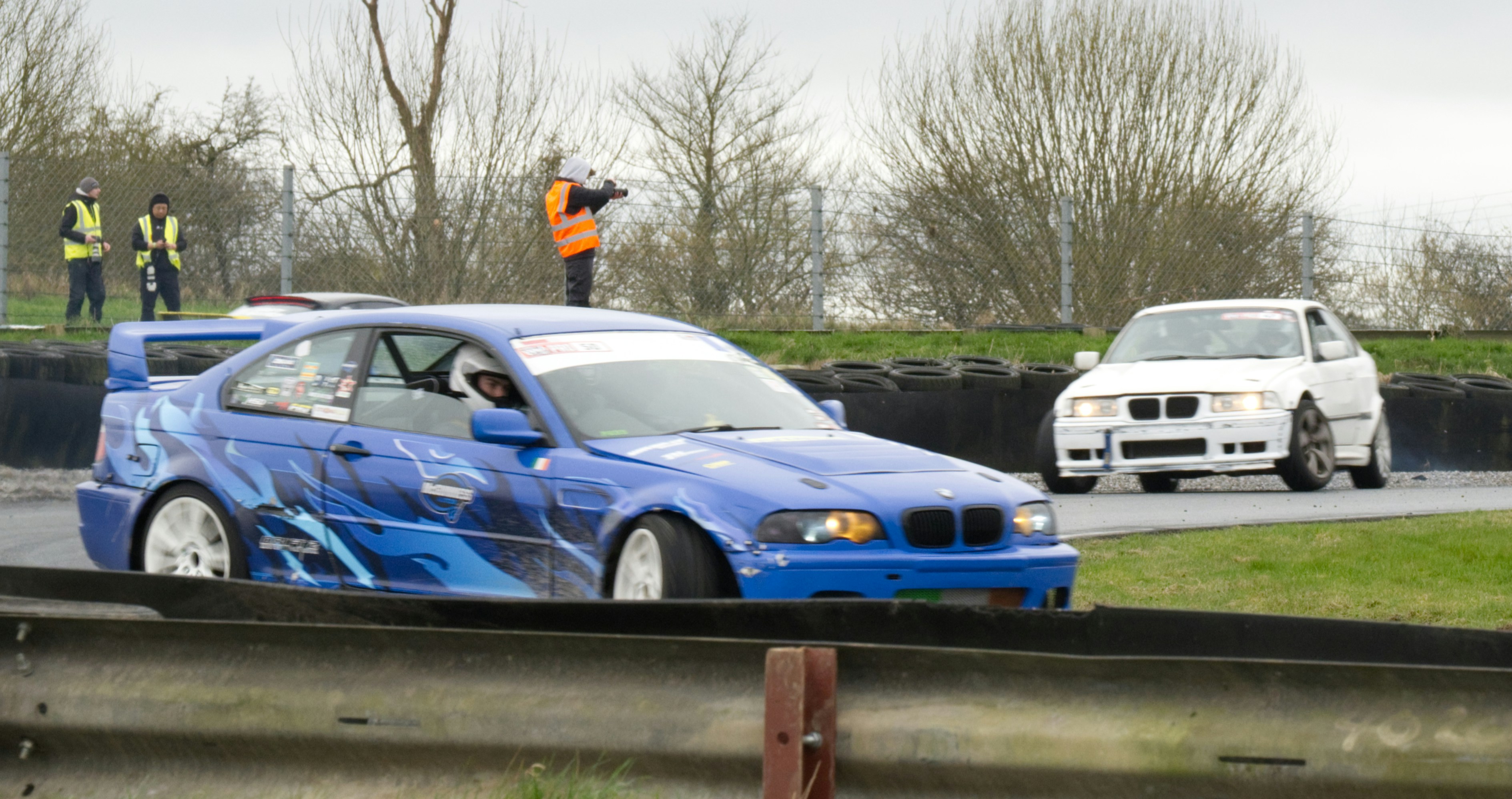 Blue race car drifting on track with white car behind.