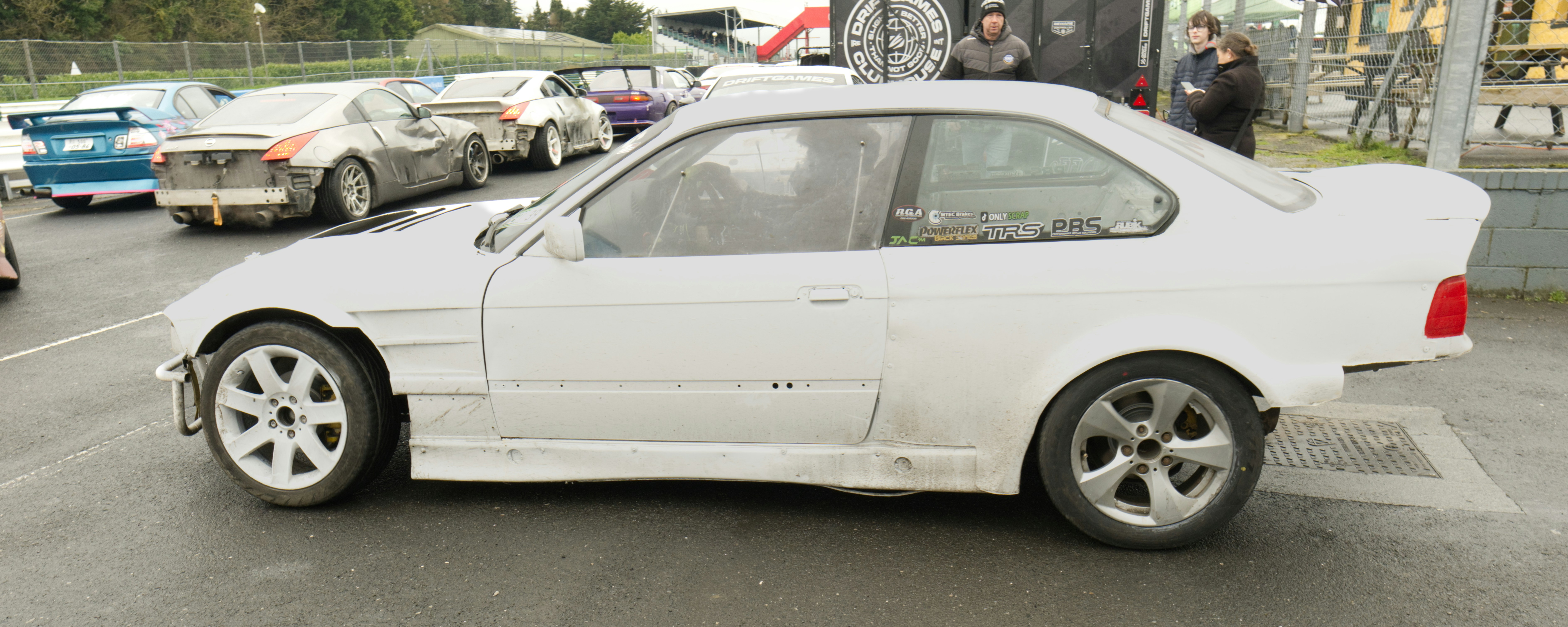 White racing car parked on asphalt with other cars behind.