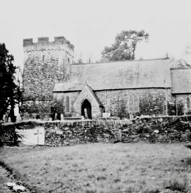 An old stone church with a square tower beside a graveyard, in black and white