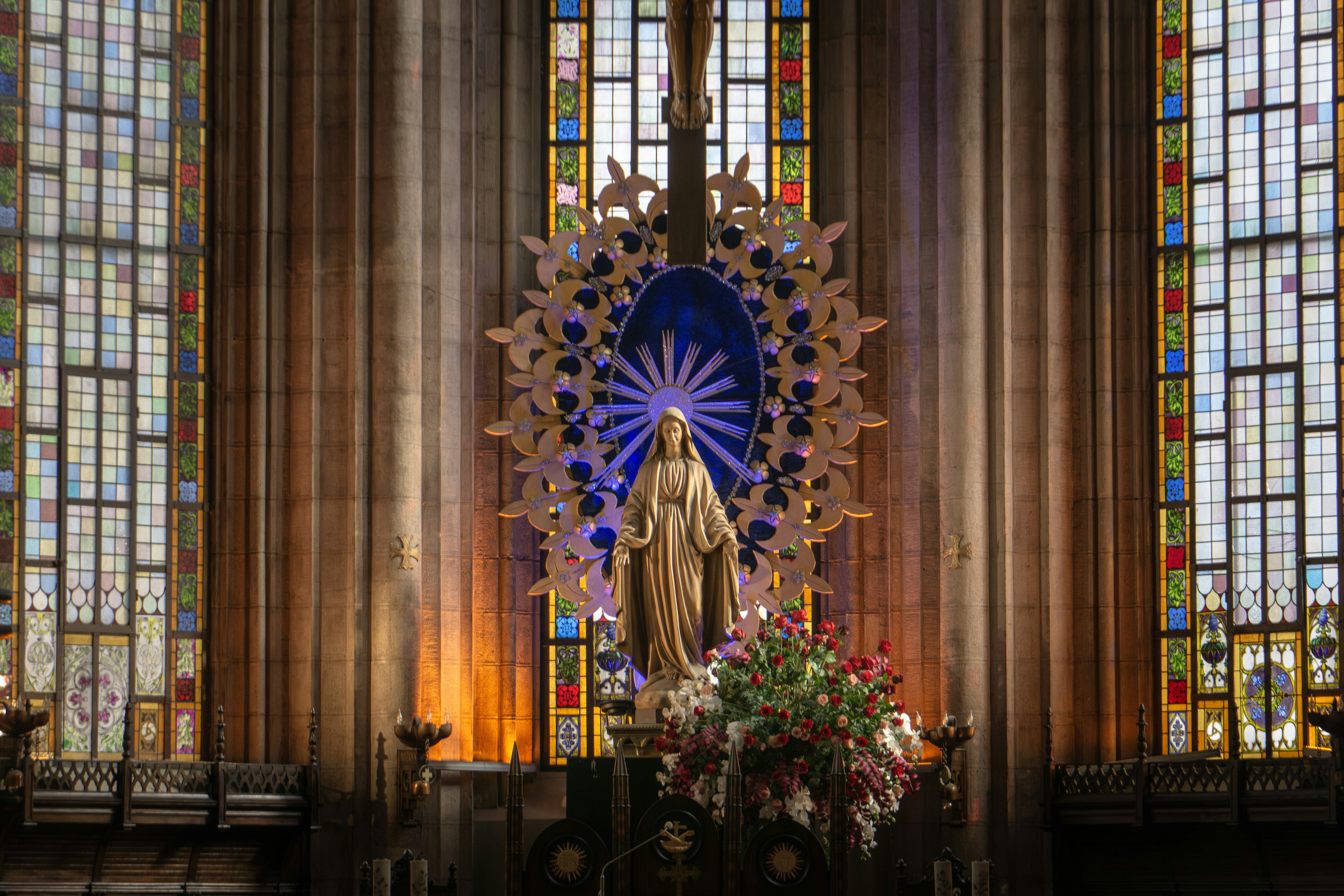 Statue of mary with stained glass windows and flowers