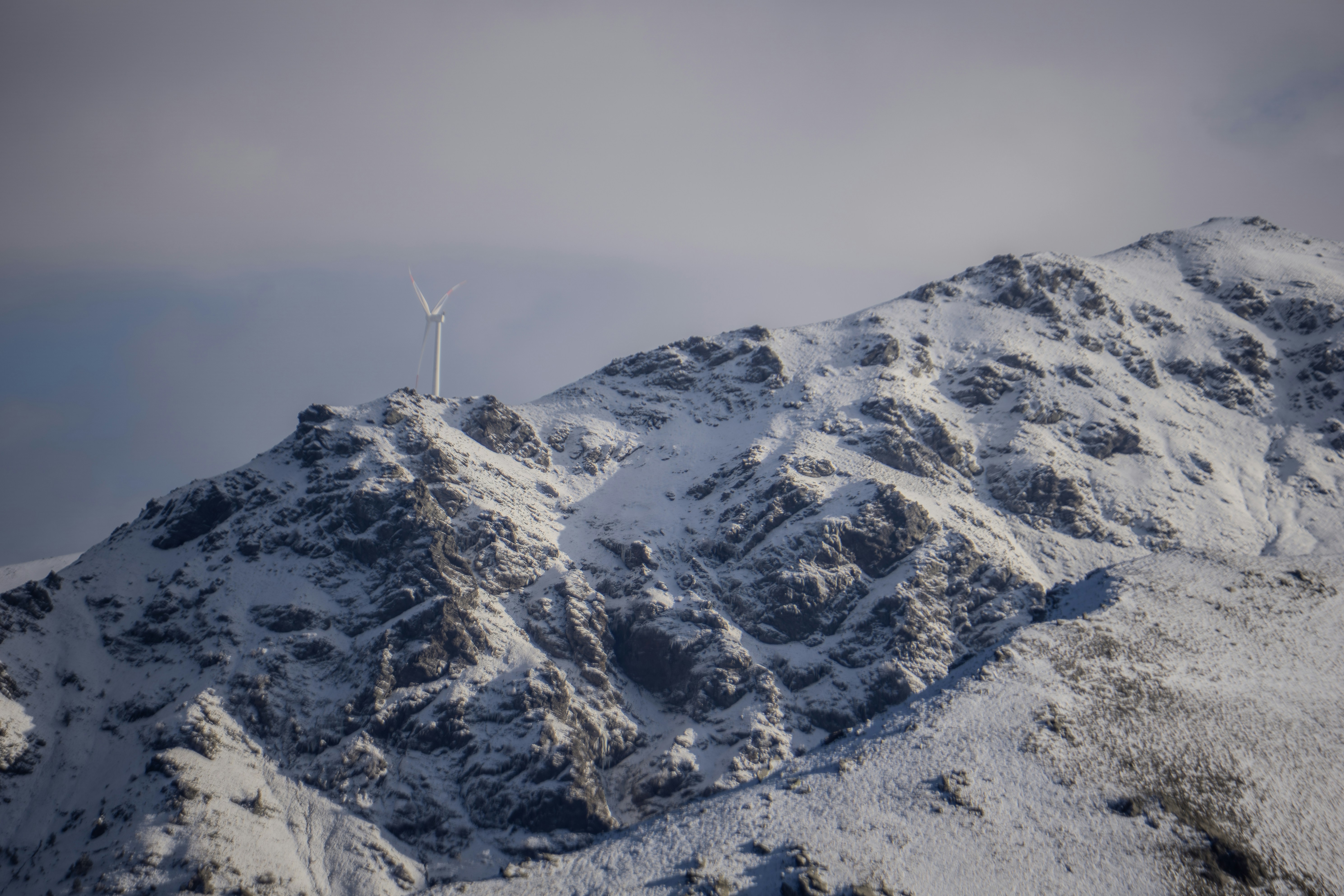 Snowy mountain peak with a distant wind turbine.
