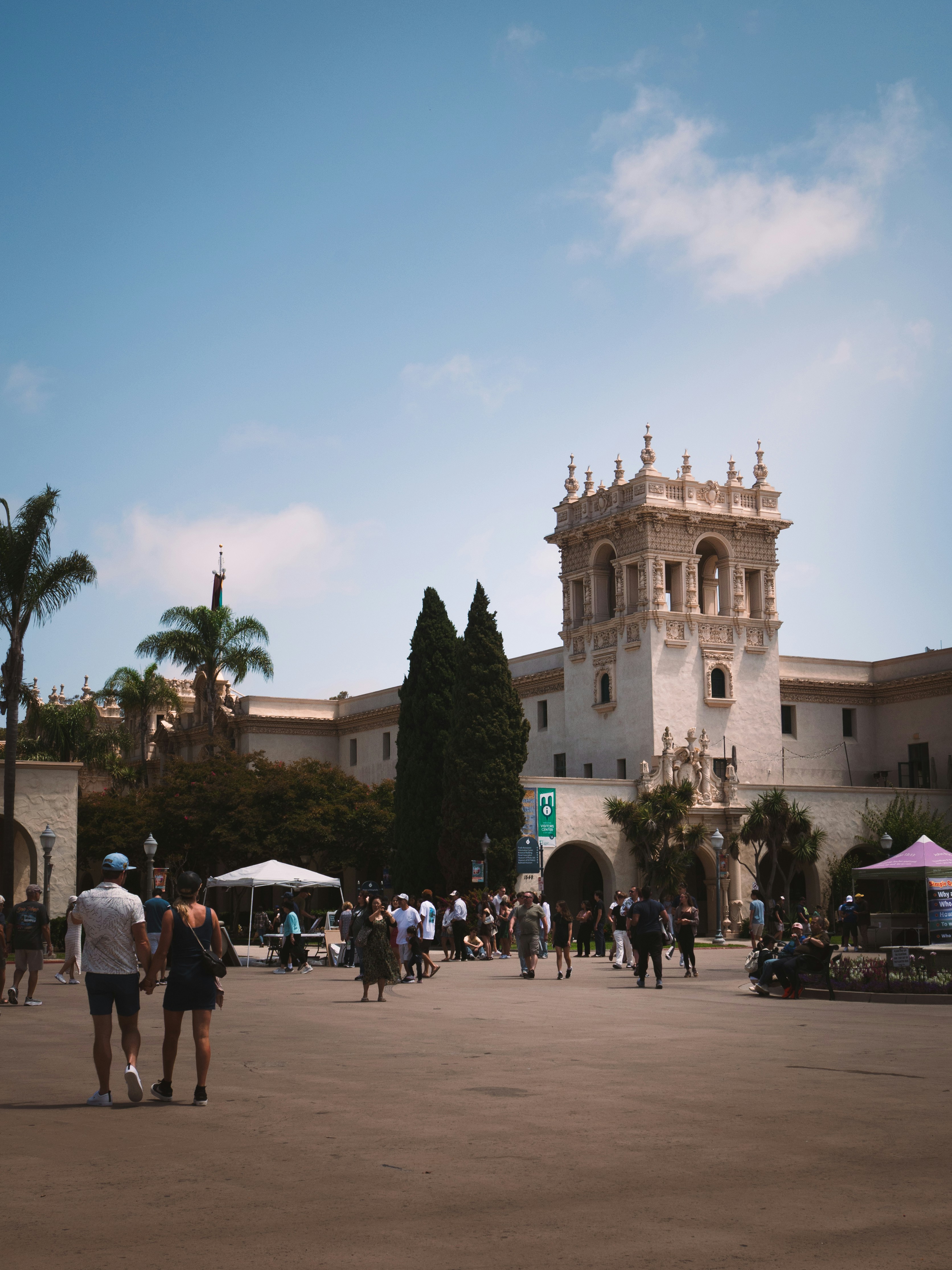 People walk around a spanish-style building on a sunny day.