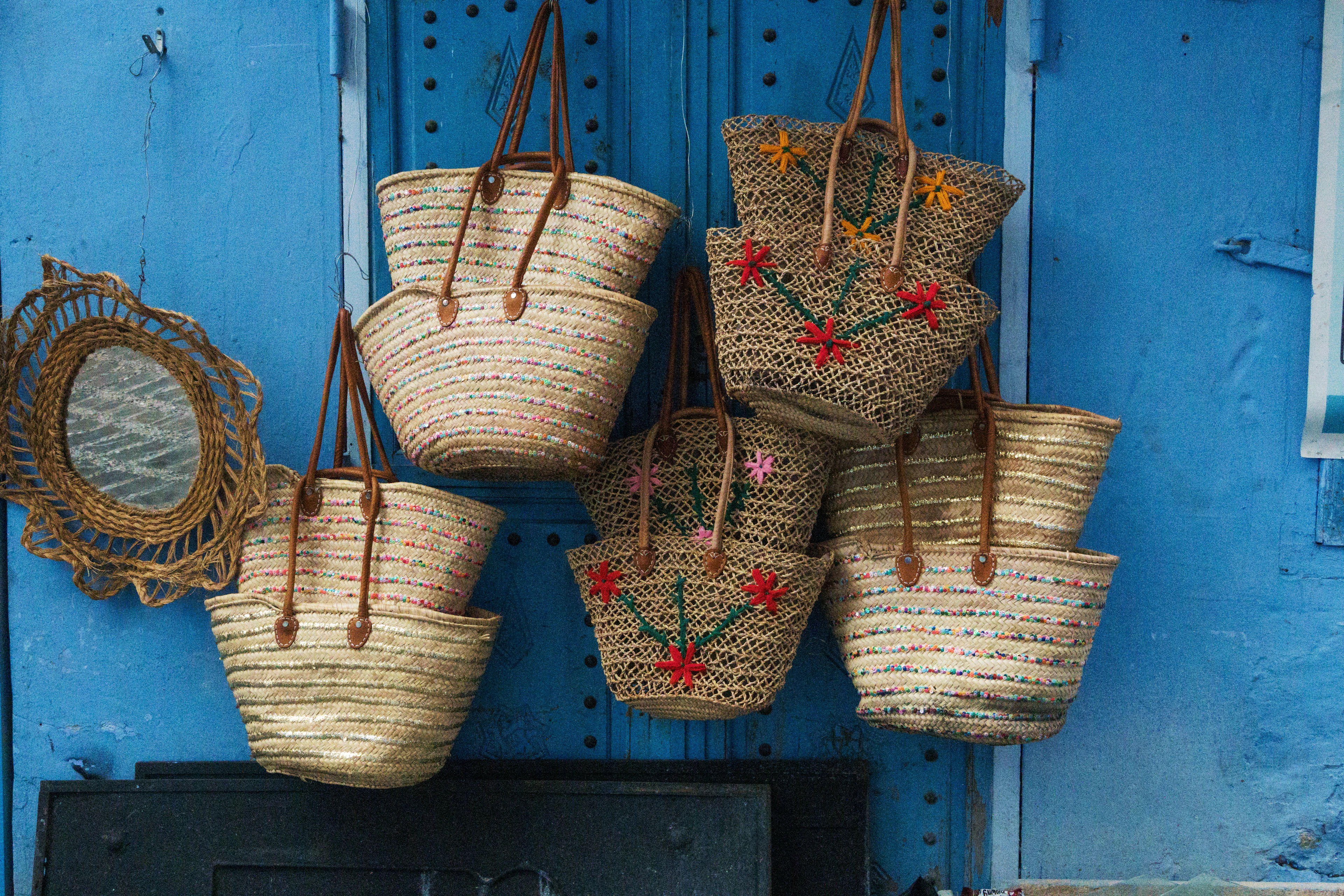 Woven straw bags with floral embroidery hanging against a blue wall.