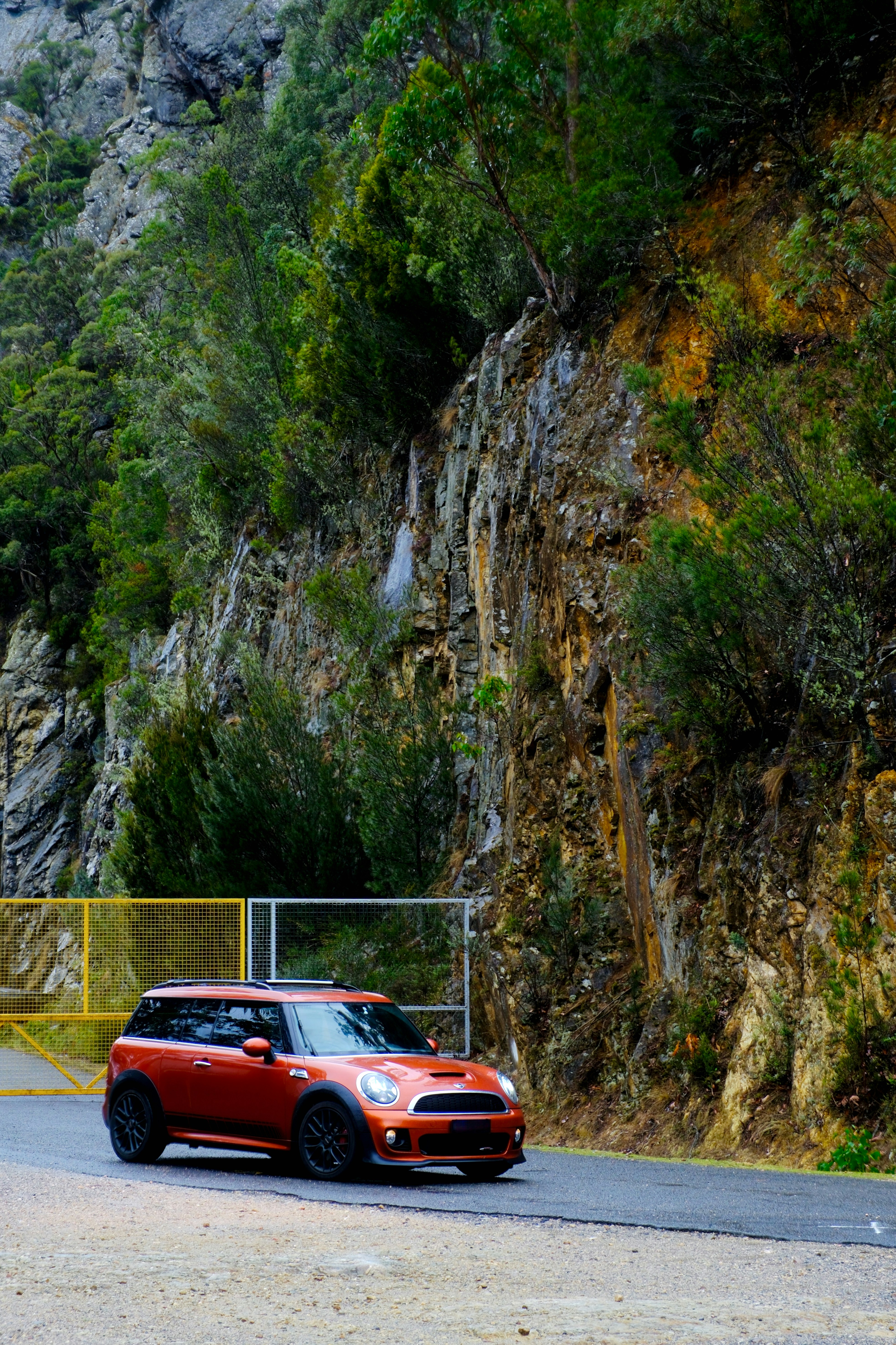 Un Mini Cooper naranja circula por una carretera de montaña.