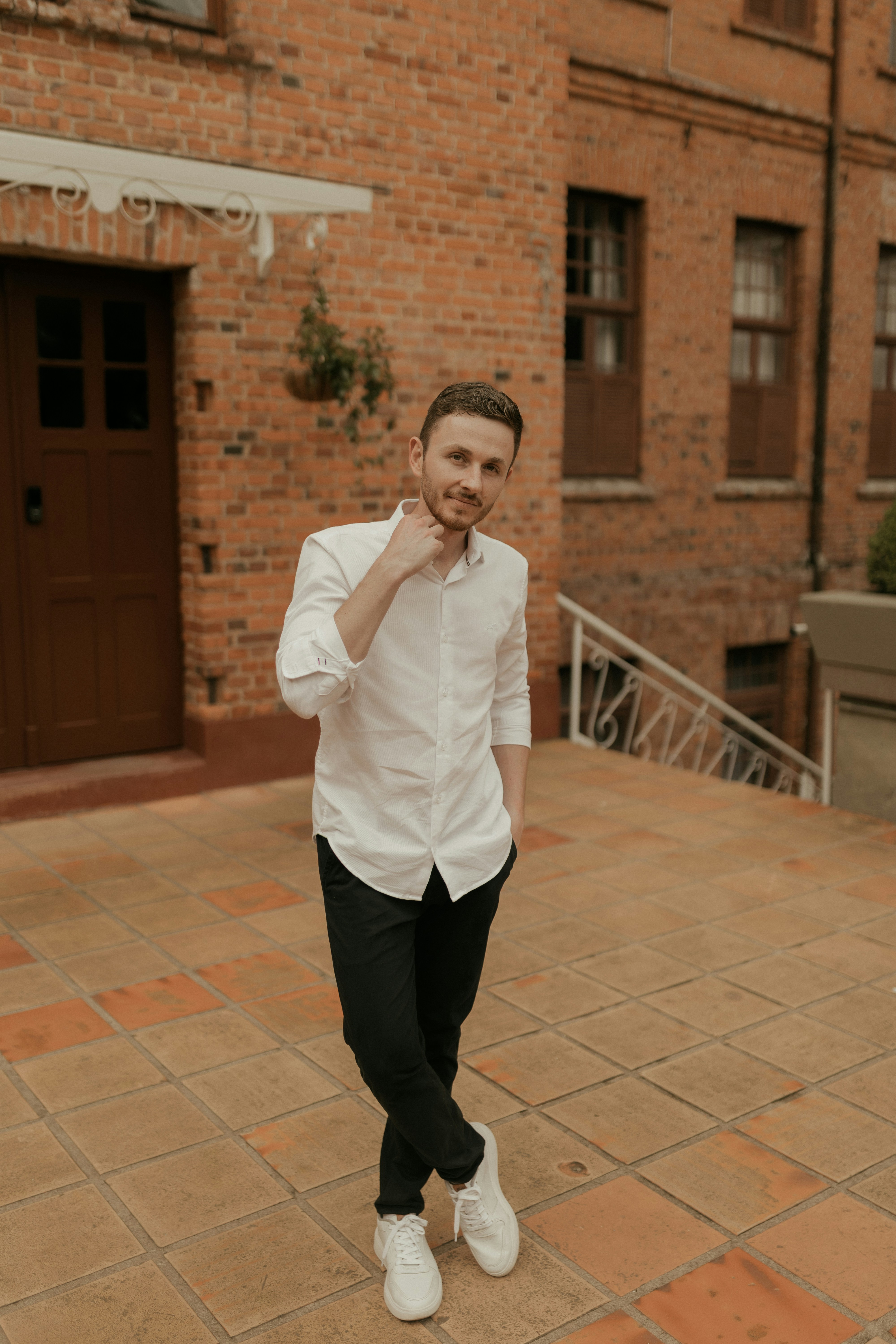 Young man in white shirt and black pants standing outside.