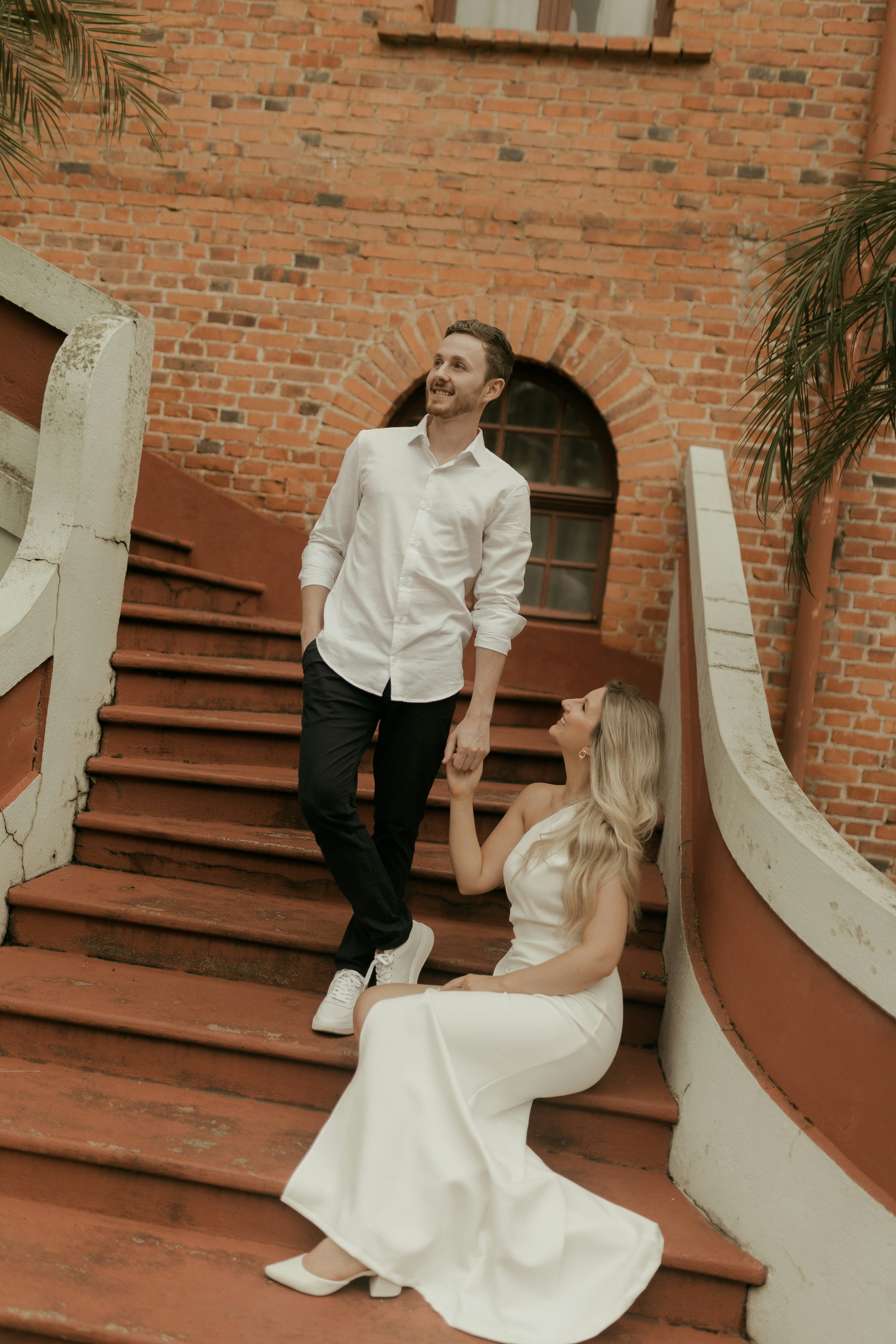 Couple holding hands on red stairs outside brick building