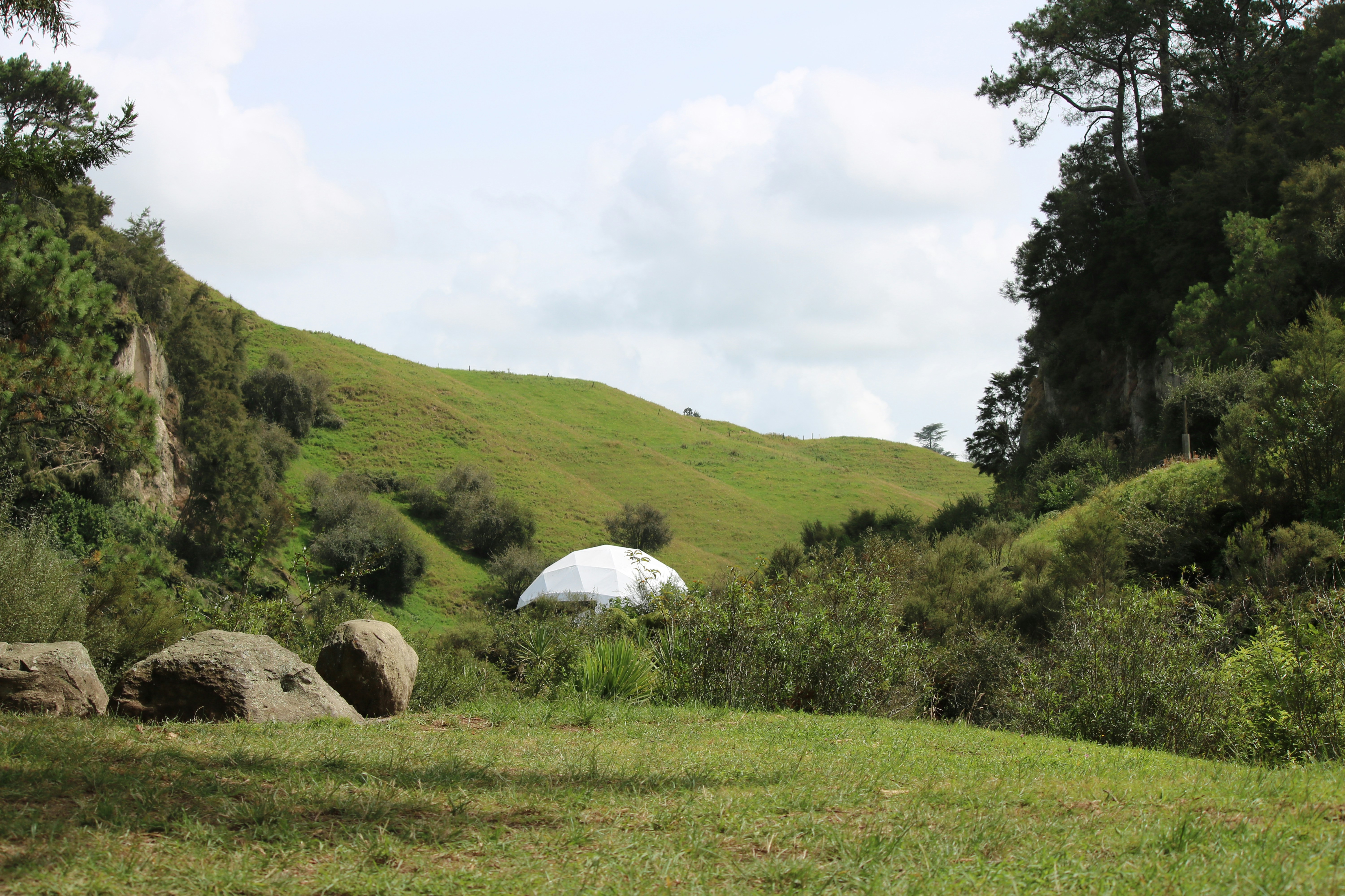 White dome structure nestled in a green, hilly landscape.