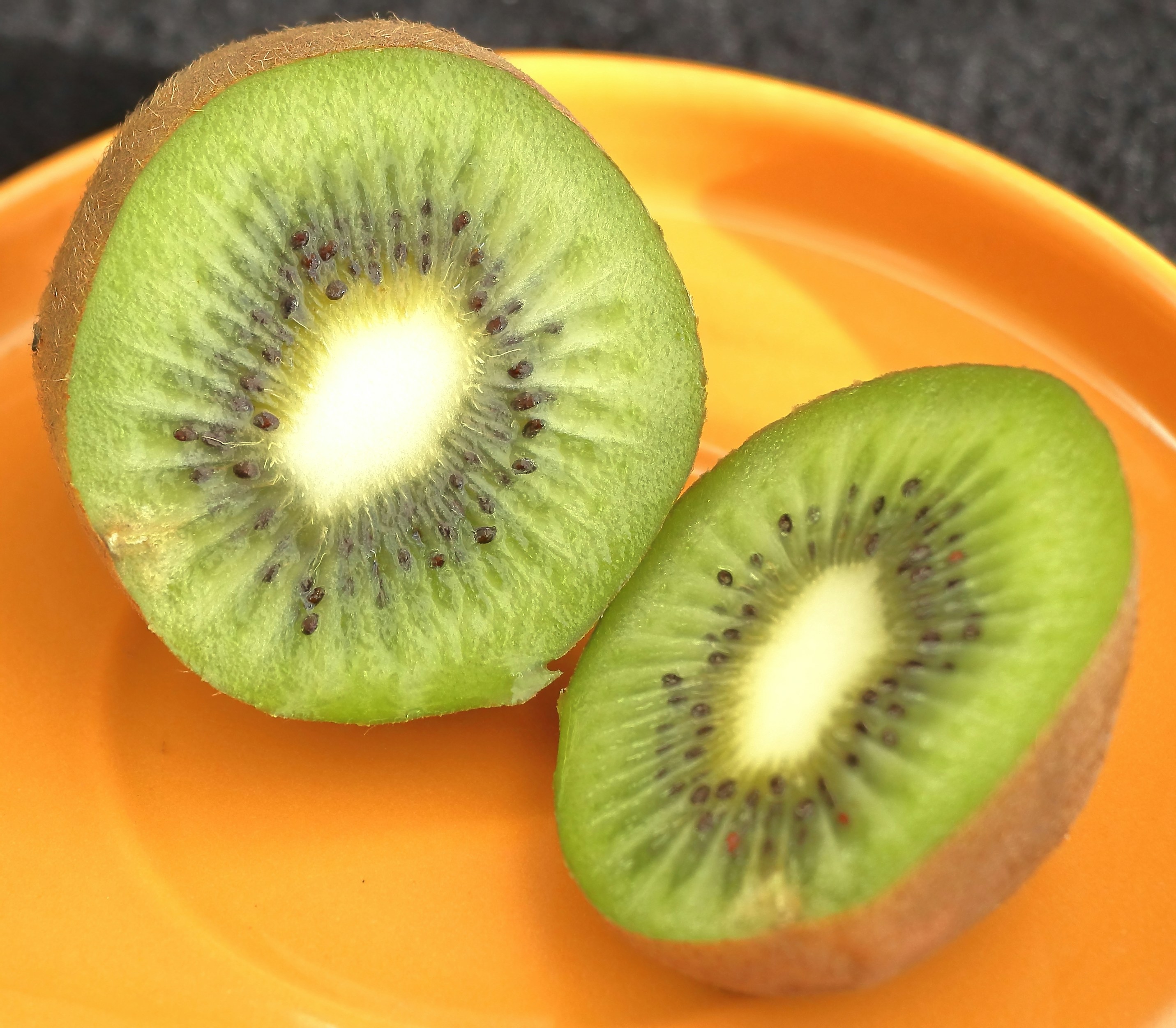 Two halves of a kiwi fruit on an orange plate