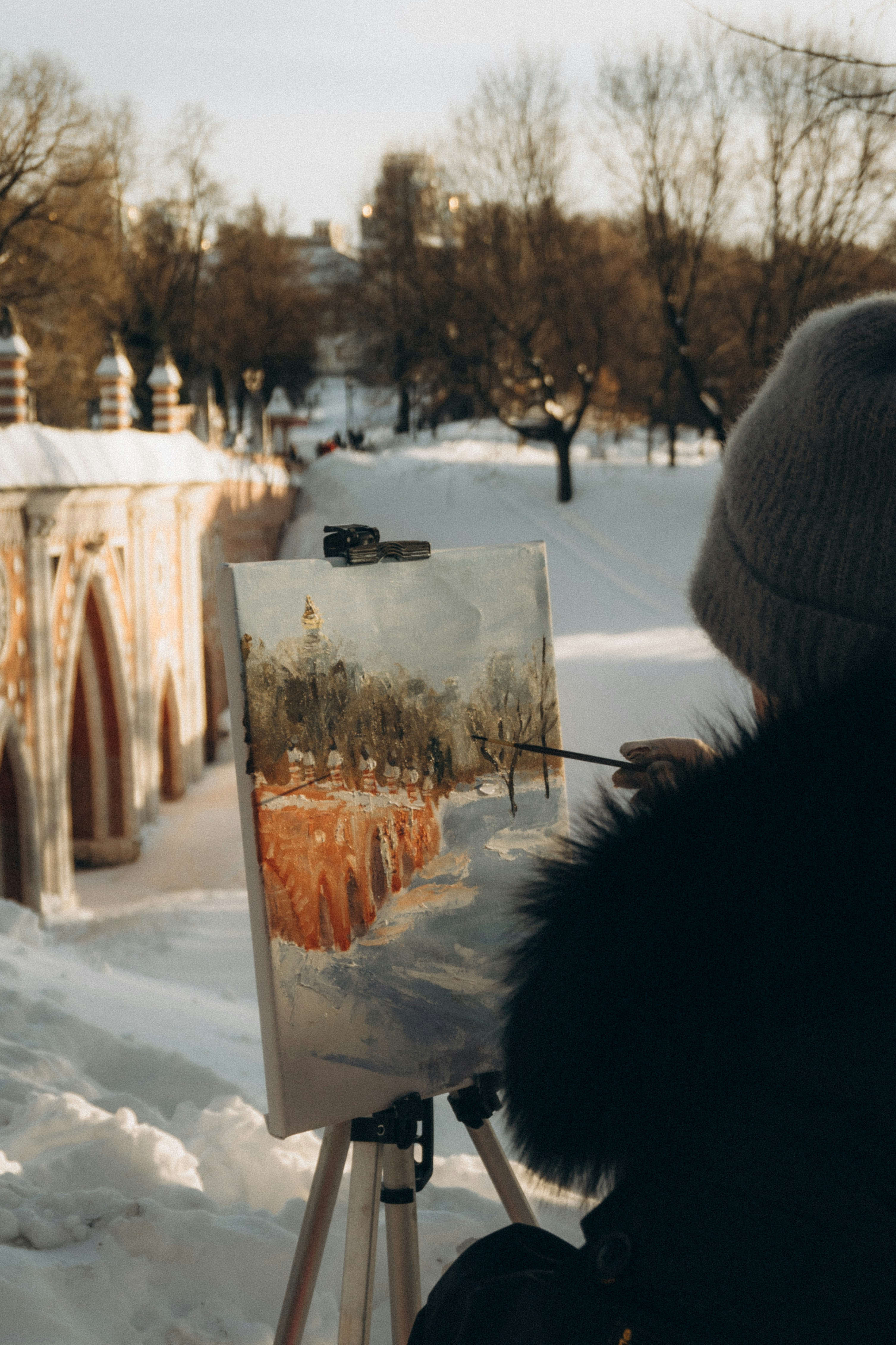 Artist painting a snowy park scene on easel.