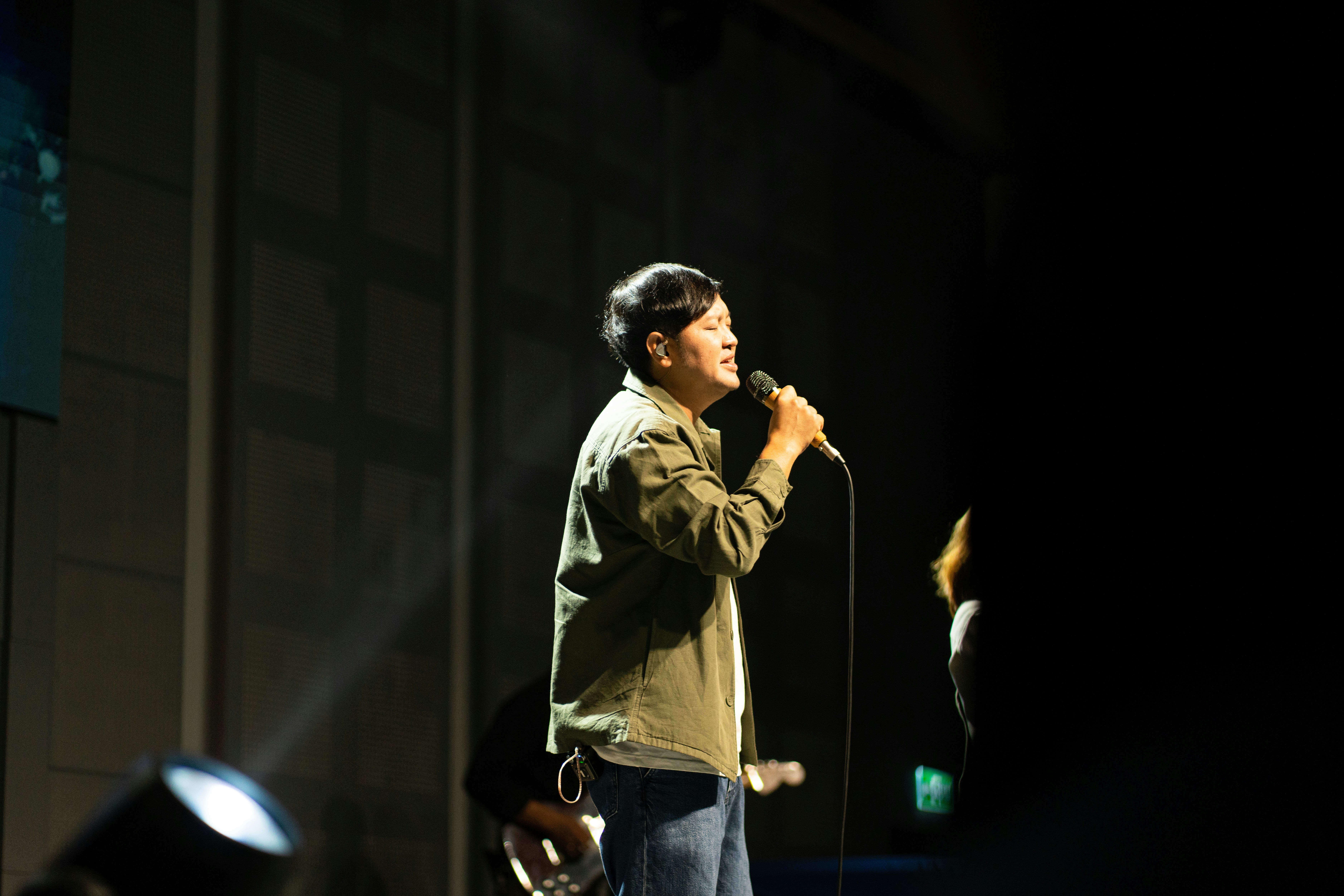 Man singing into a microphone on a dark stage.