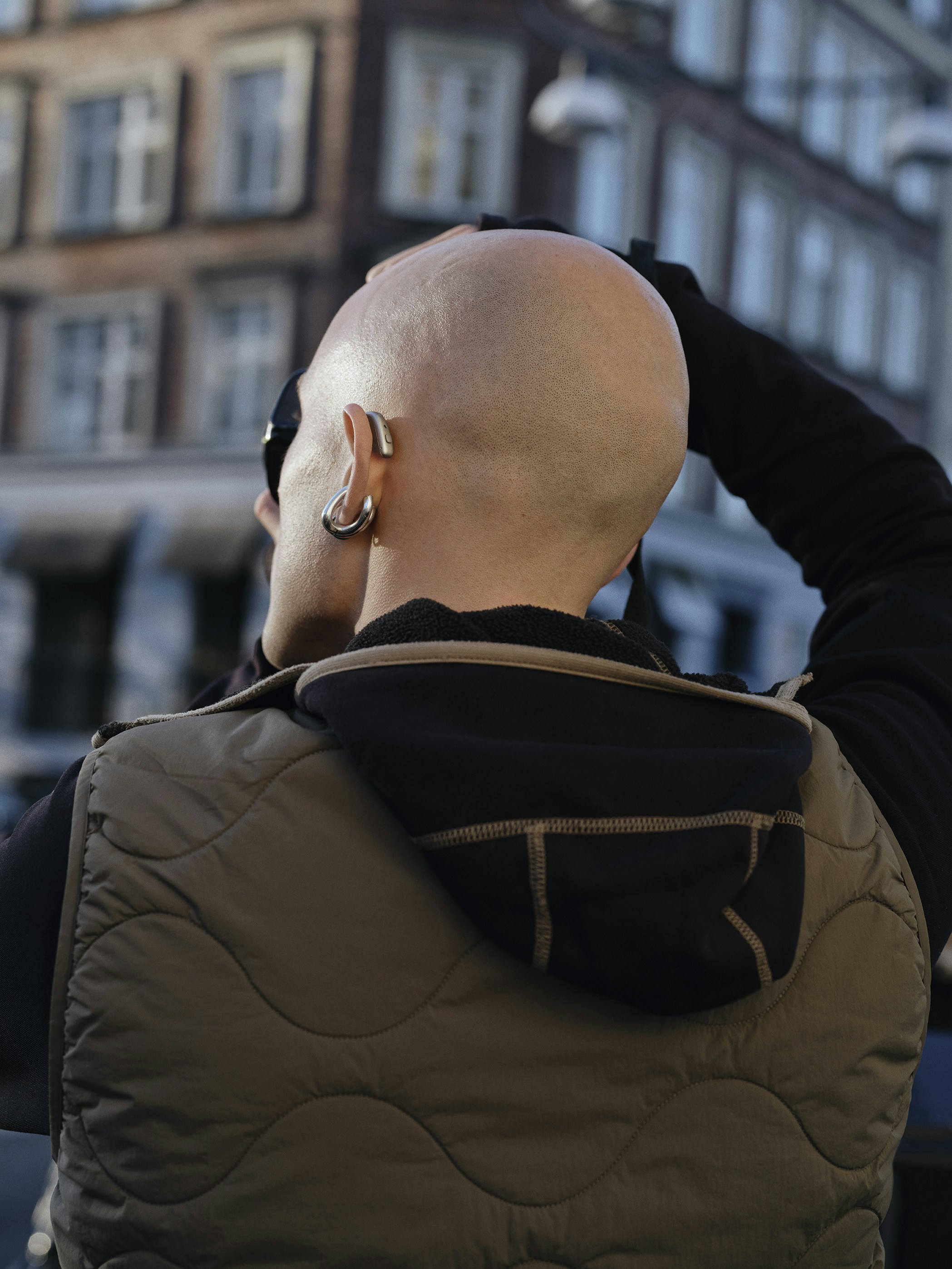 Bald person in vest looking up at buildings