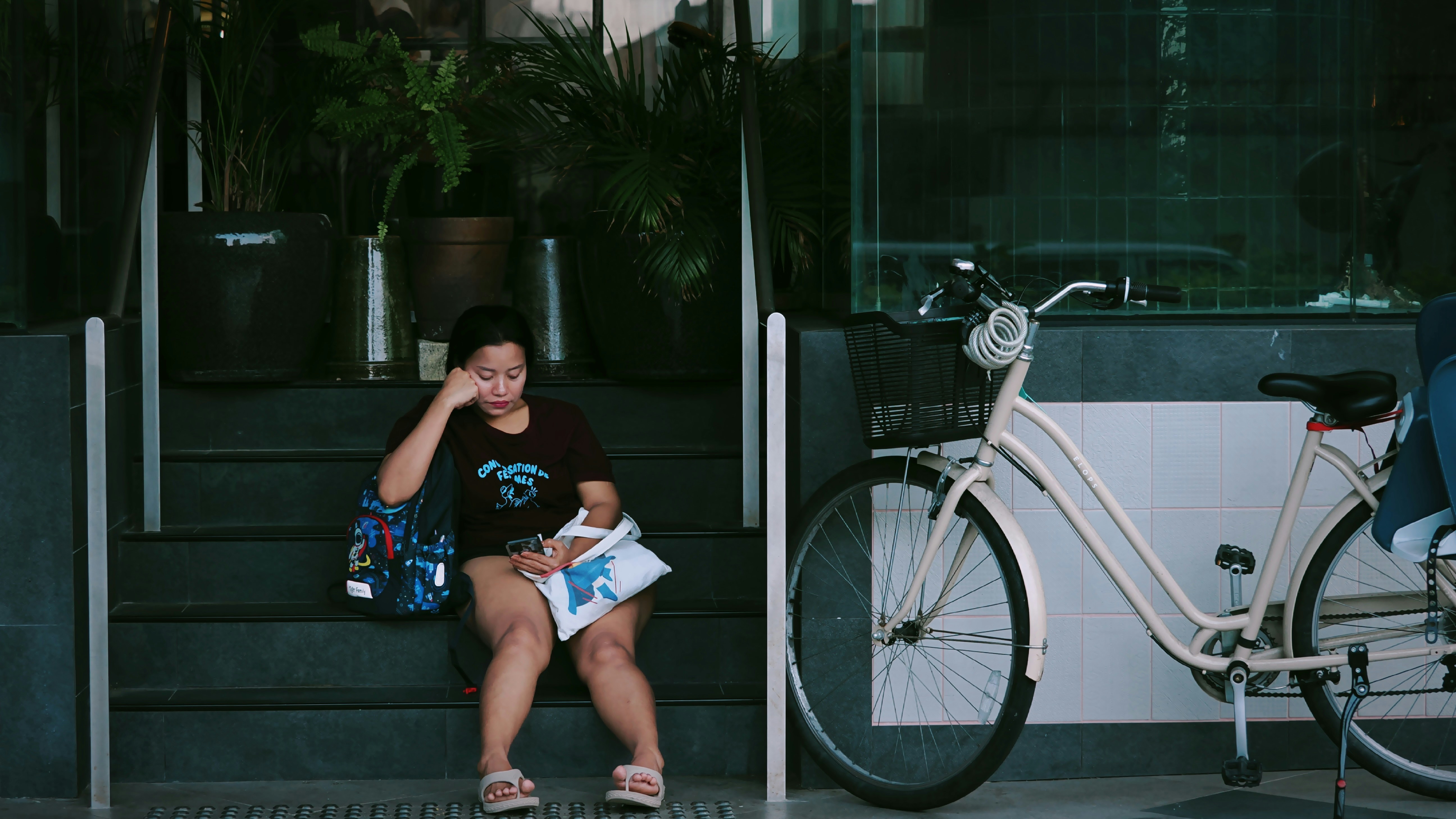 Woman sitting on steps next to a bicycle.