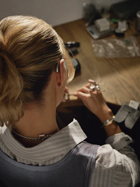 Woman working on jewelry at a wooden desk.