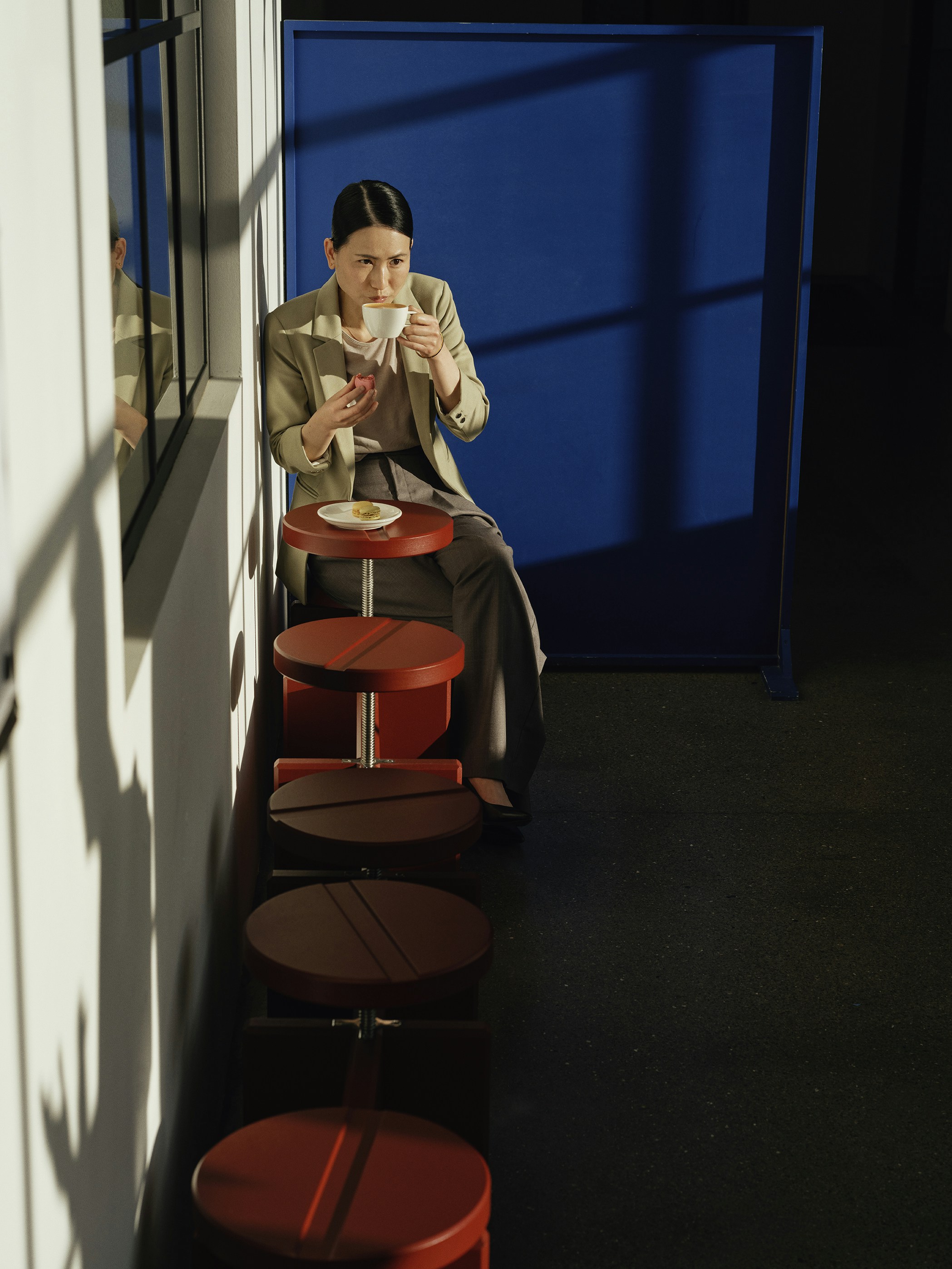 Woman drinking coffee while sitting on a stool.