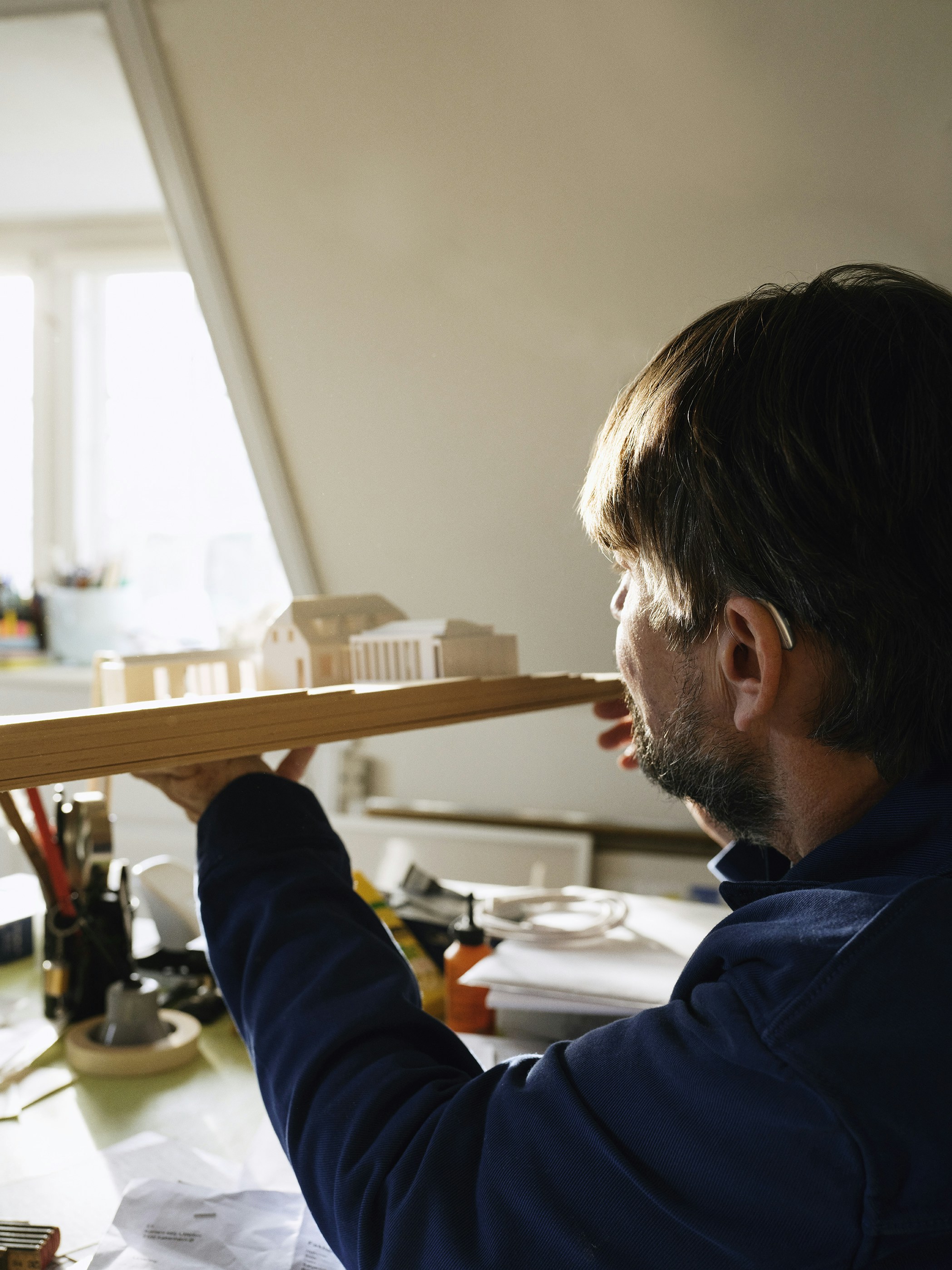 Architect examines a wooden building model on desk.