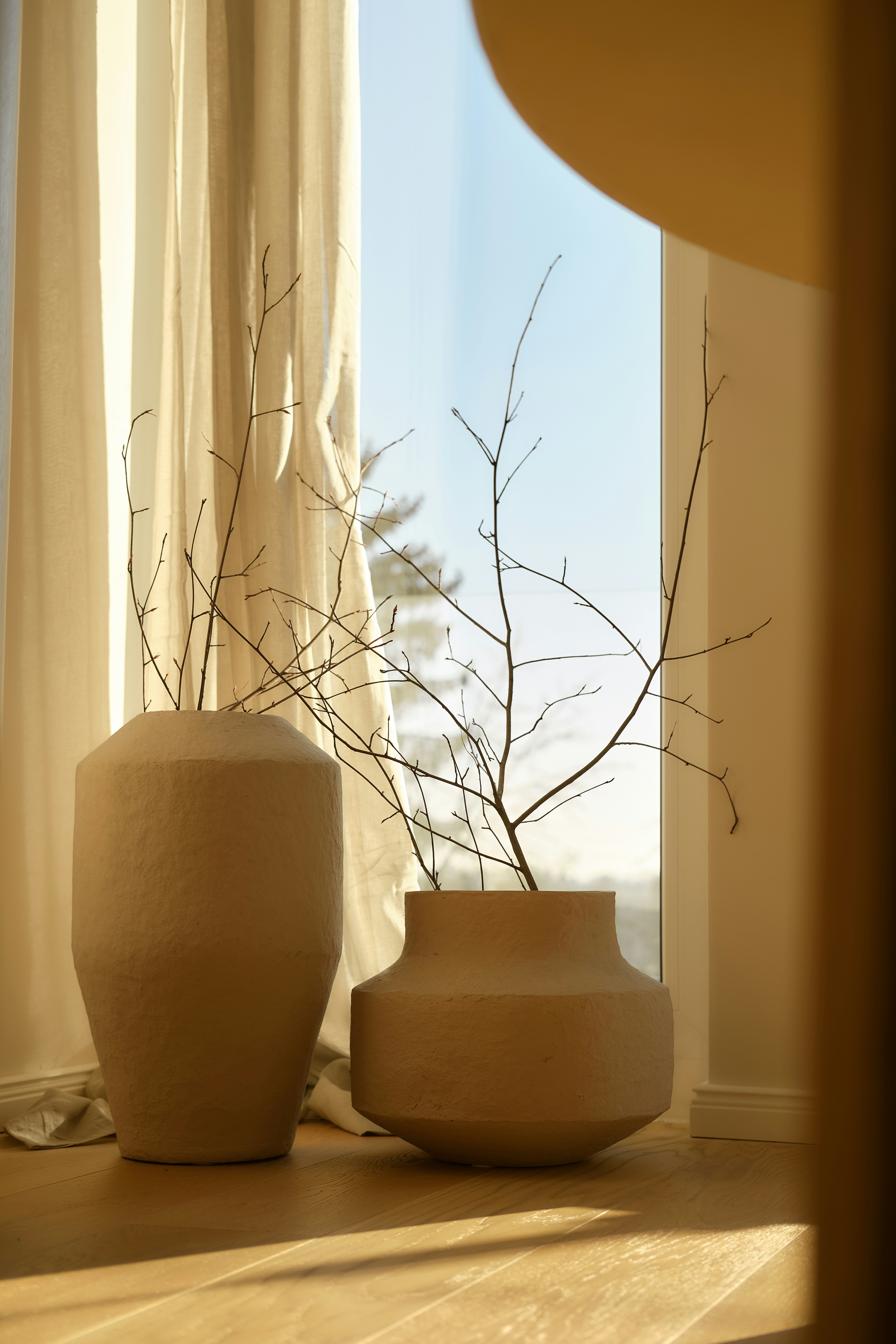Deux vases texturés avec des branches sèches près de la fenêtre.